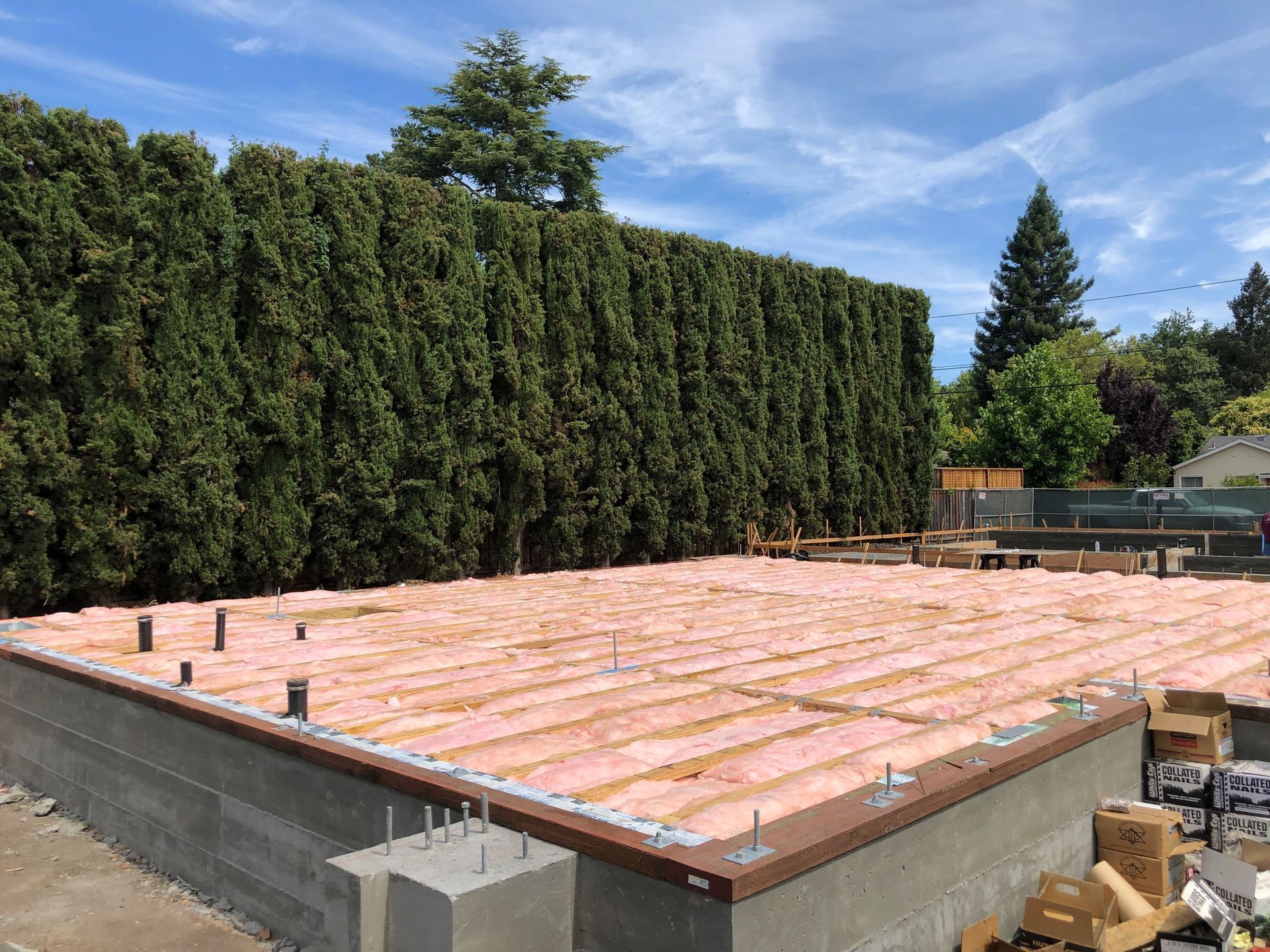 Flat roof under construction with pink insulation boards and green hedges in the background