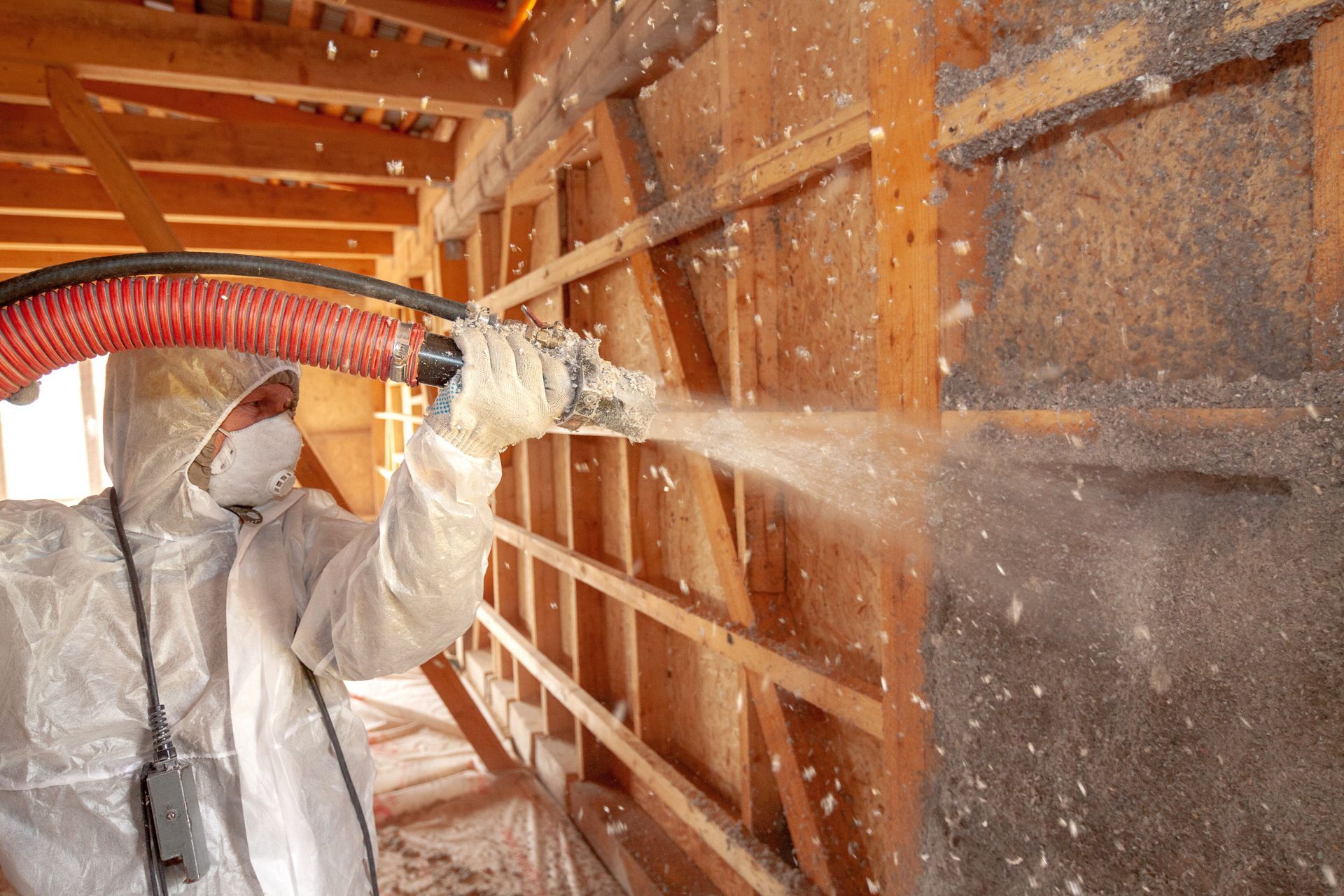Worker in protective suit spray-foaming insulation inside a wooden attic frame