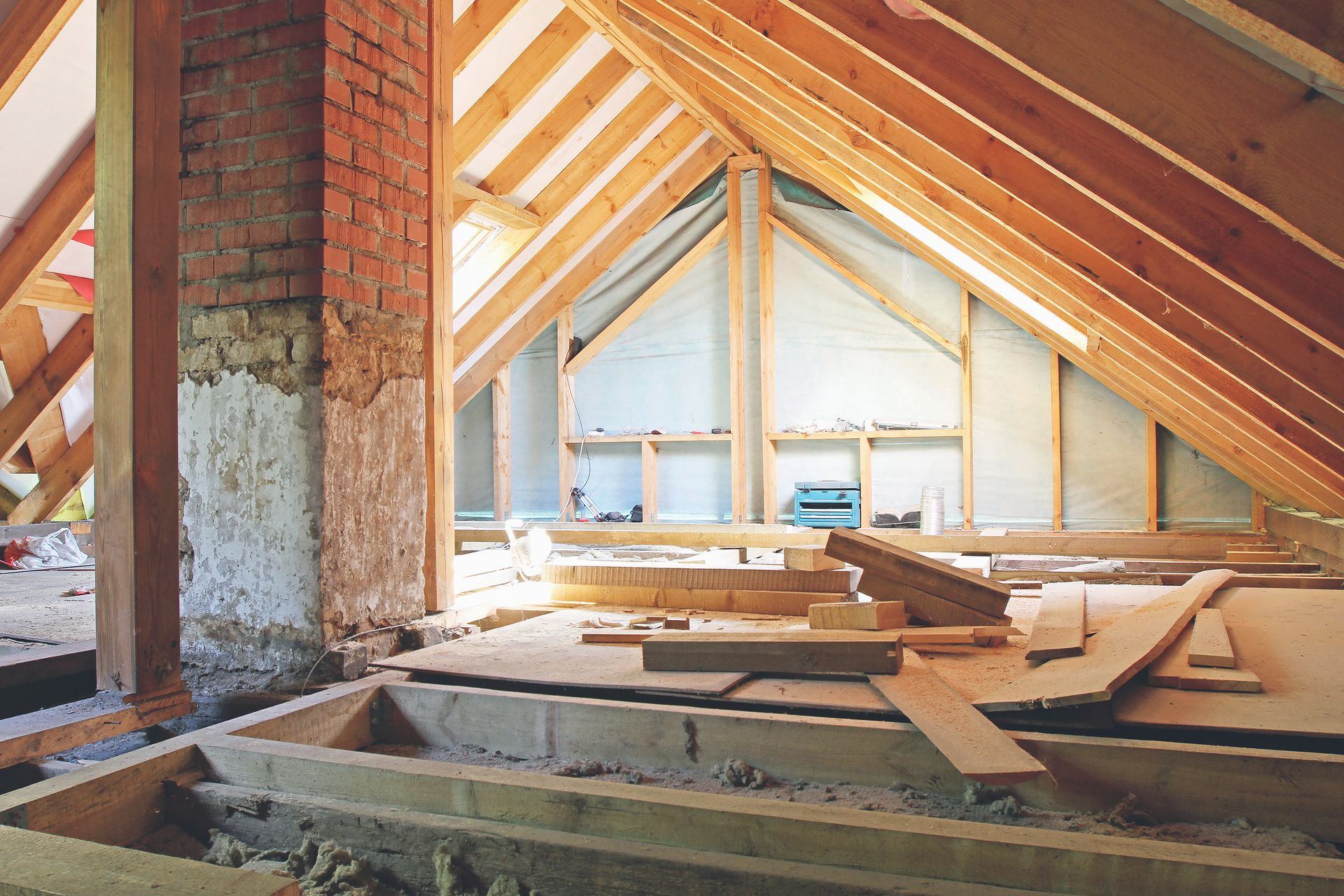 Attic under construction with exposed wooden beams, brick chimney, and insulation boards on the floor