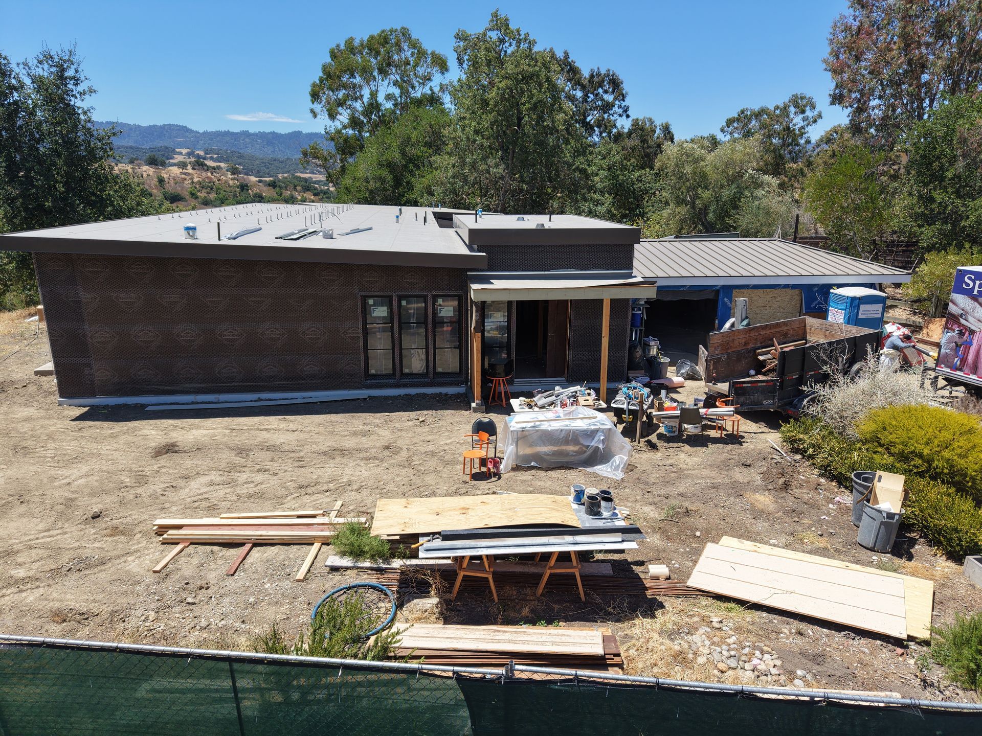 Single-story house under construction with lumber, tools, and debris in a dry yard.