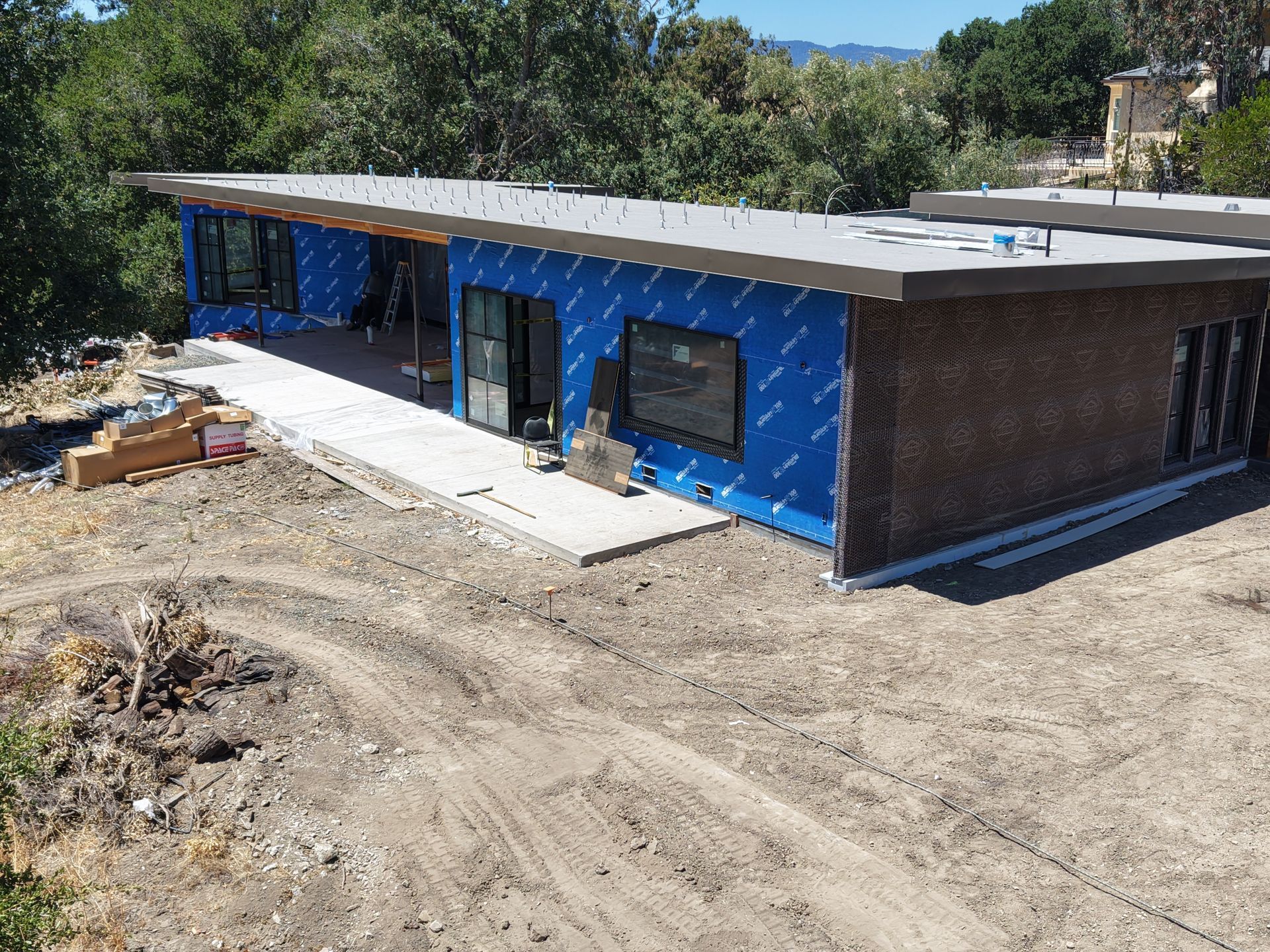 Blue single-story building under construction on a dirt lot, viewed from the front-left side.