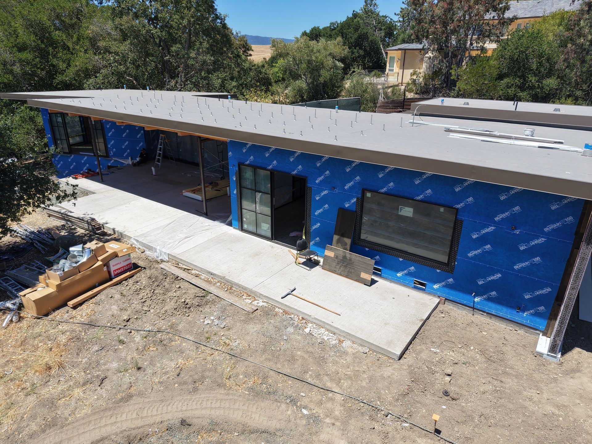 Blue house under construction with a long sloped roof and concrete walkway in front