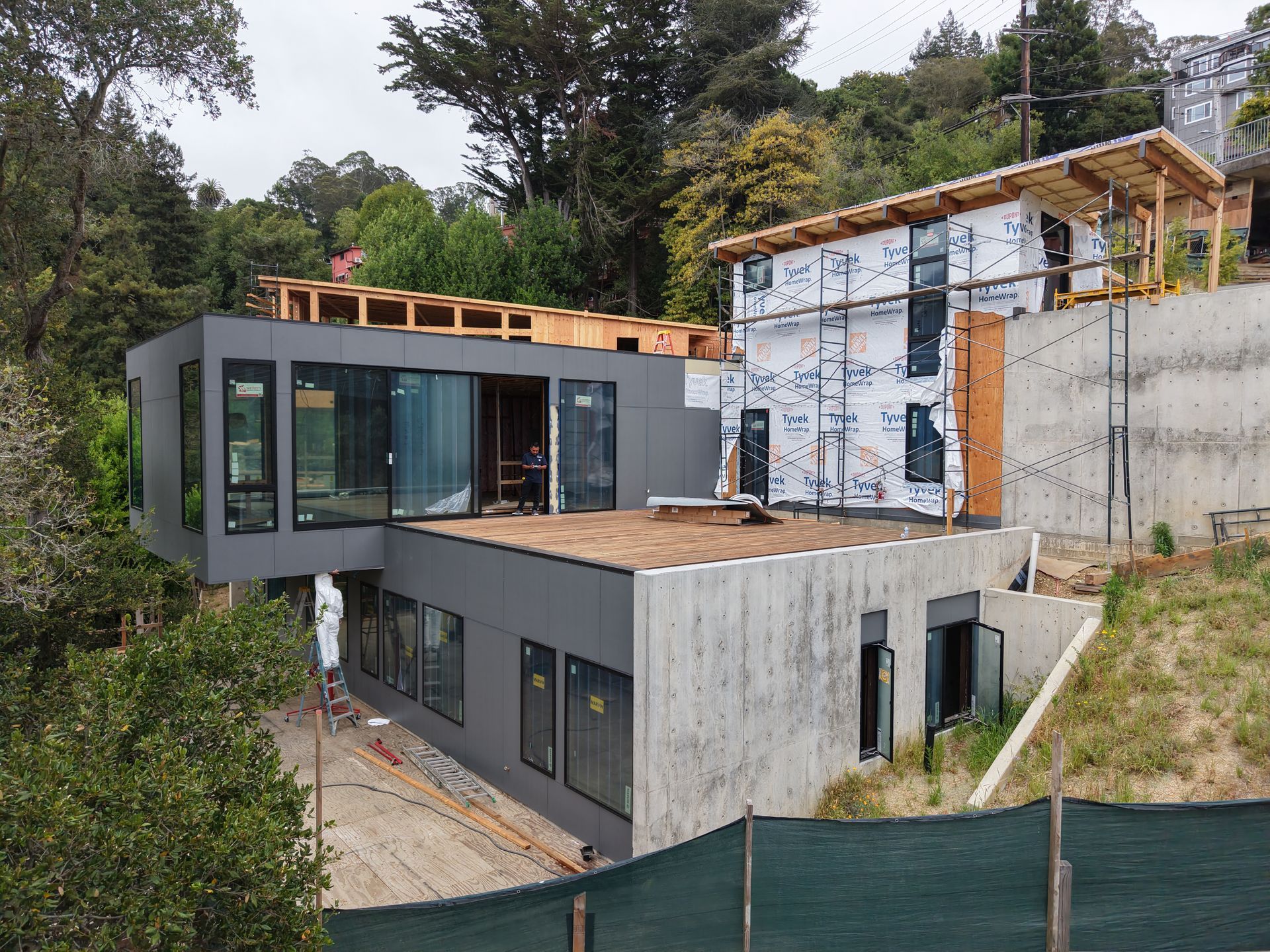Modern concrete hillside house under construction with large windows and exposed framing