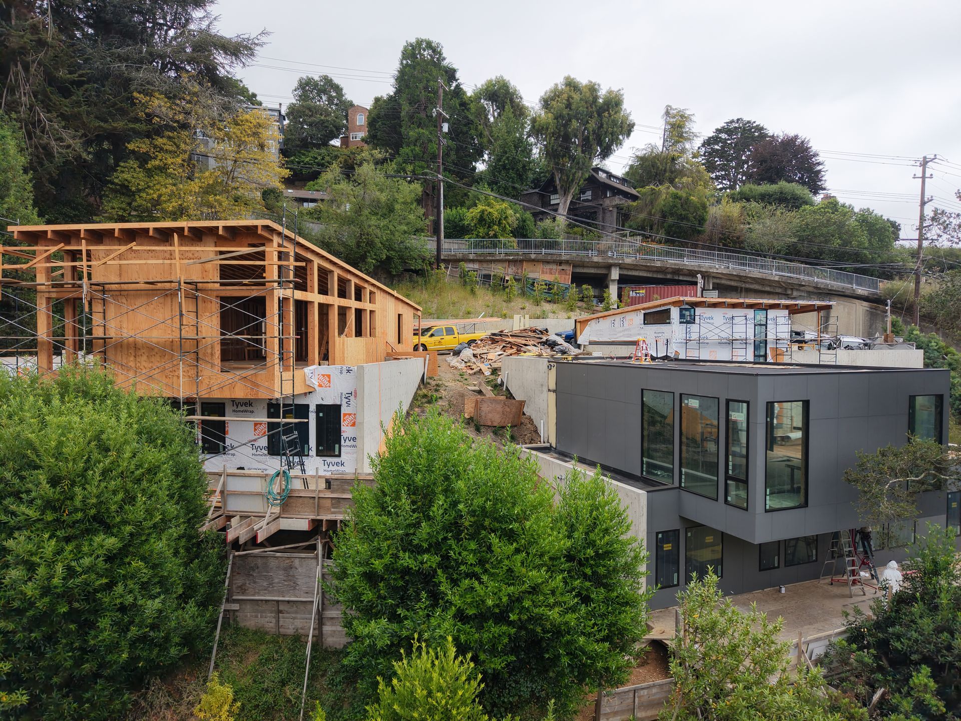 Residential buildings under construction on a hillside, with a gray modern house in the foreground.