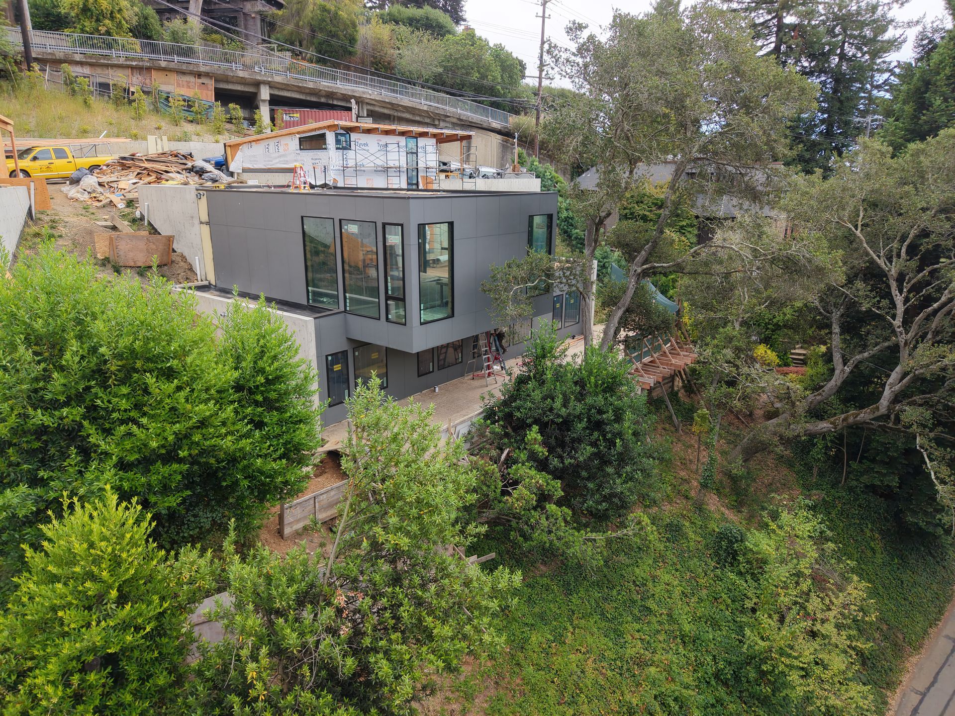 Modern gray house with large windows on a wooded hillside, overlooking lush greenery