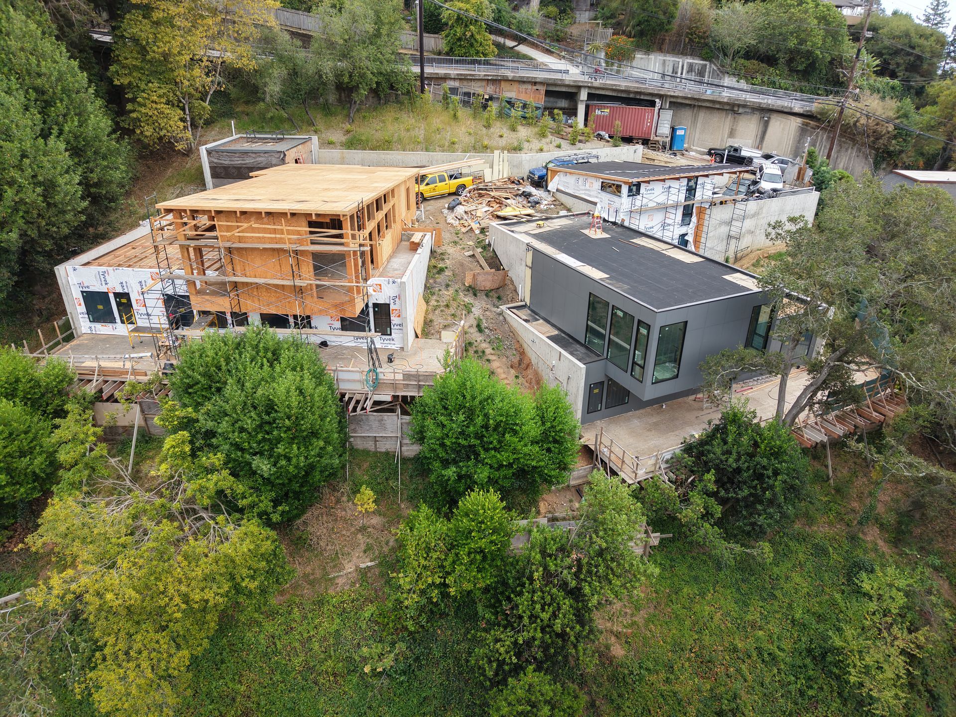 Aerial view of two modern houses under construction surrounded by trees and hillside greenery