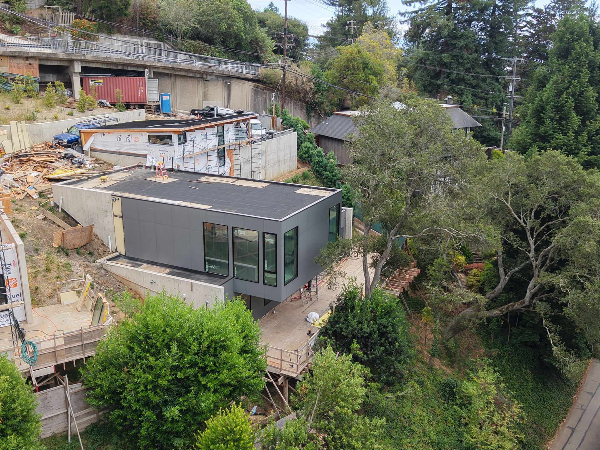 Modern gray house on a steep hillside with trees and construction debris nearby