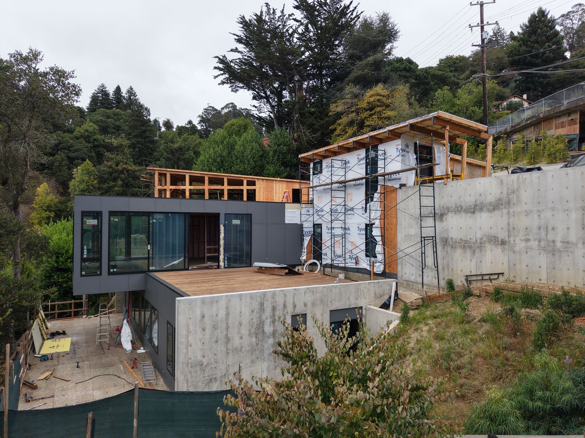 Modern house under construction on a steep hillside with concrete walls and surrounding trees