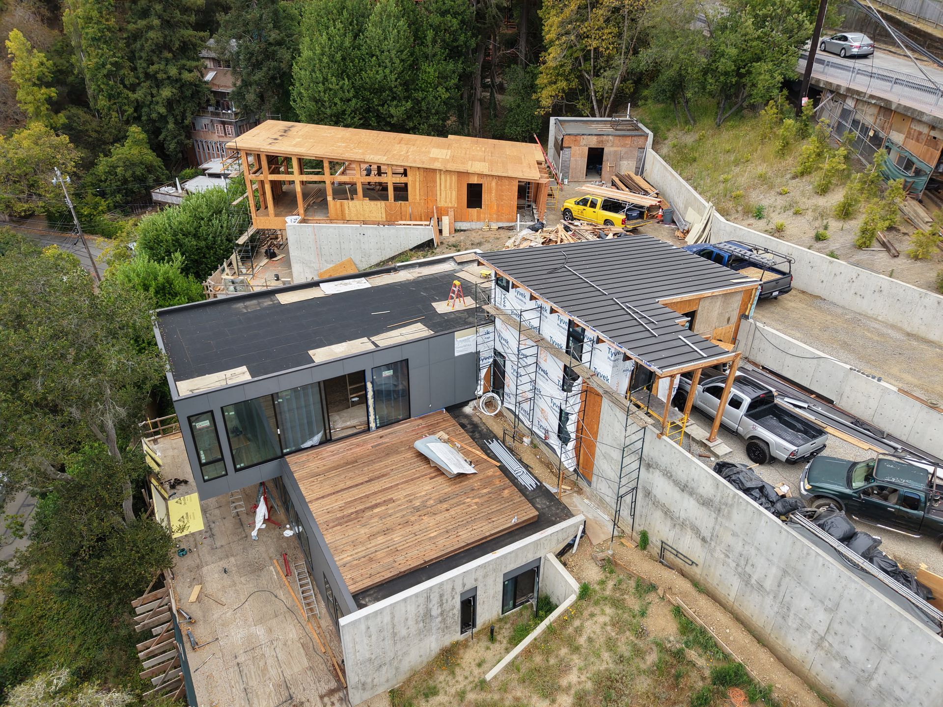 Aerial view of a modern house under construction with rooftops, wooden framing, and a hillside setting.