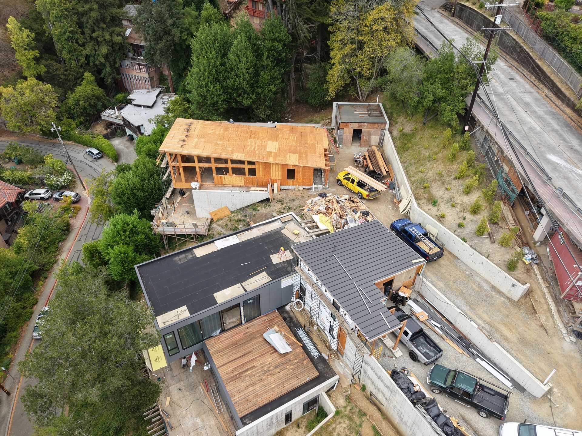 Aerial view of a house construction site with two buildings, heavy equipment, and building materials nearby.