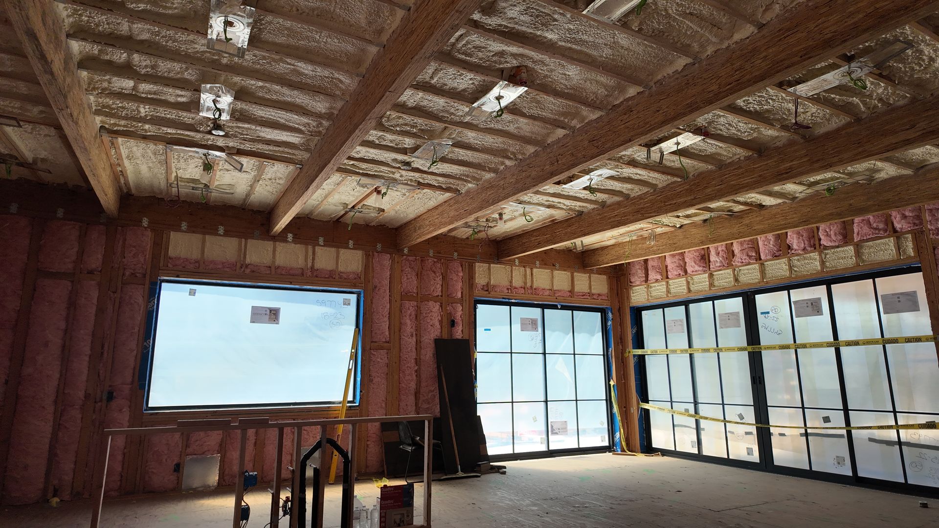 Unfinished room with exposed wood framing, large windows, and bright daylight streaming in.