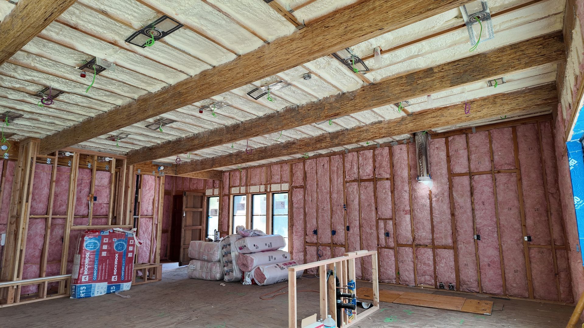 Unfinished room with exposed insulation, pink walls, stacked materials, and a hanging light bulb
