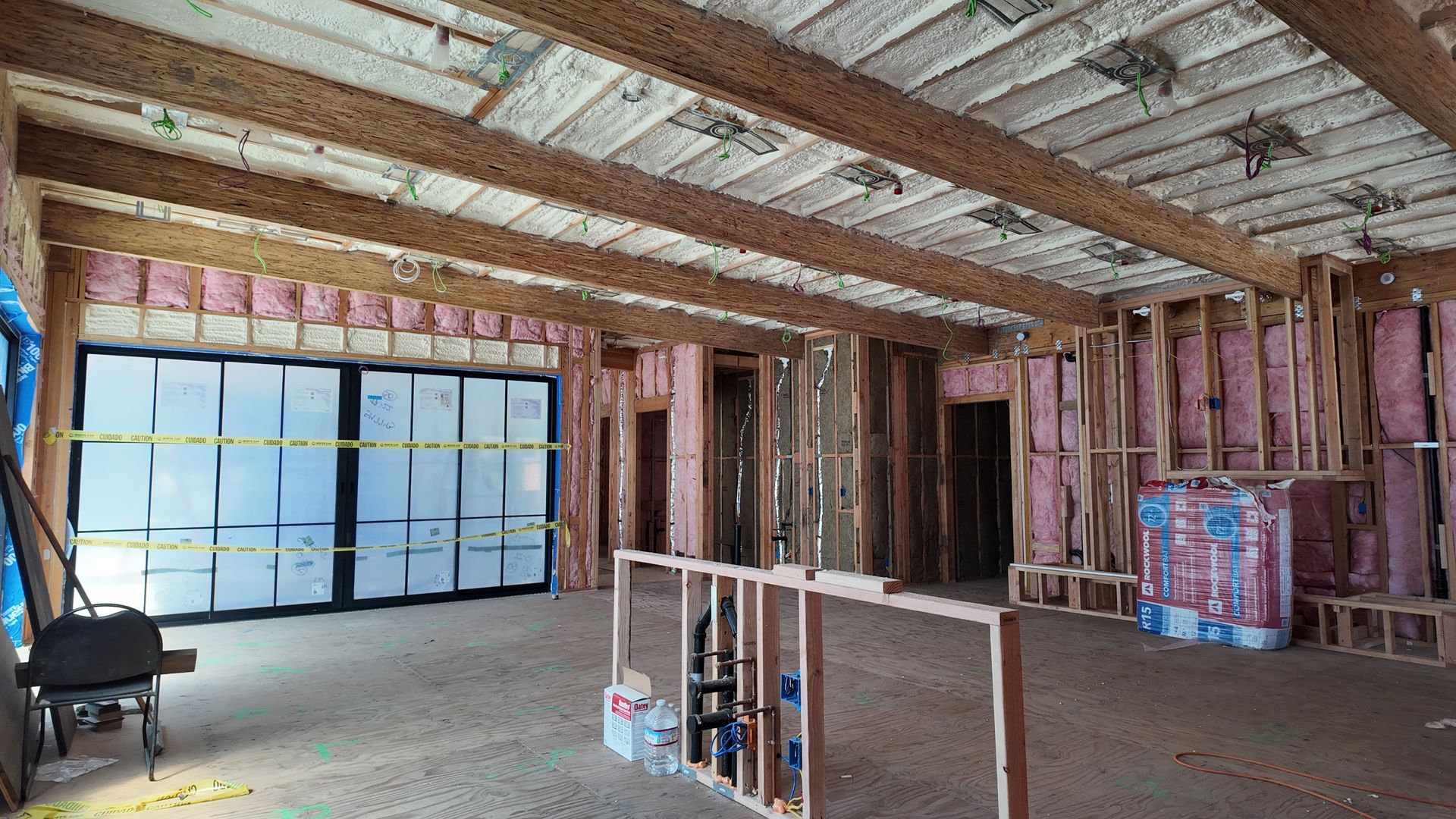 Unfinished interior with exposed wooden framing, insulation, and a wide frosted window wall.