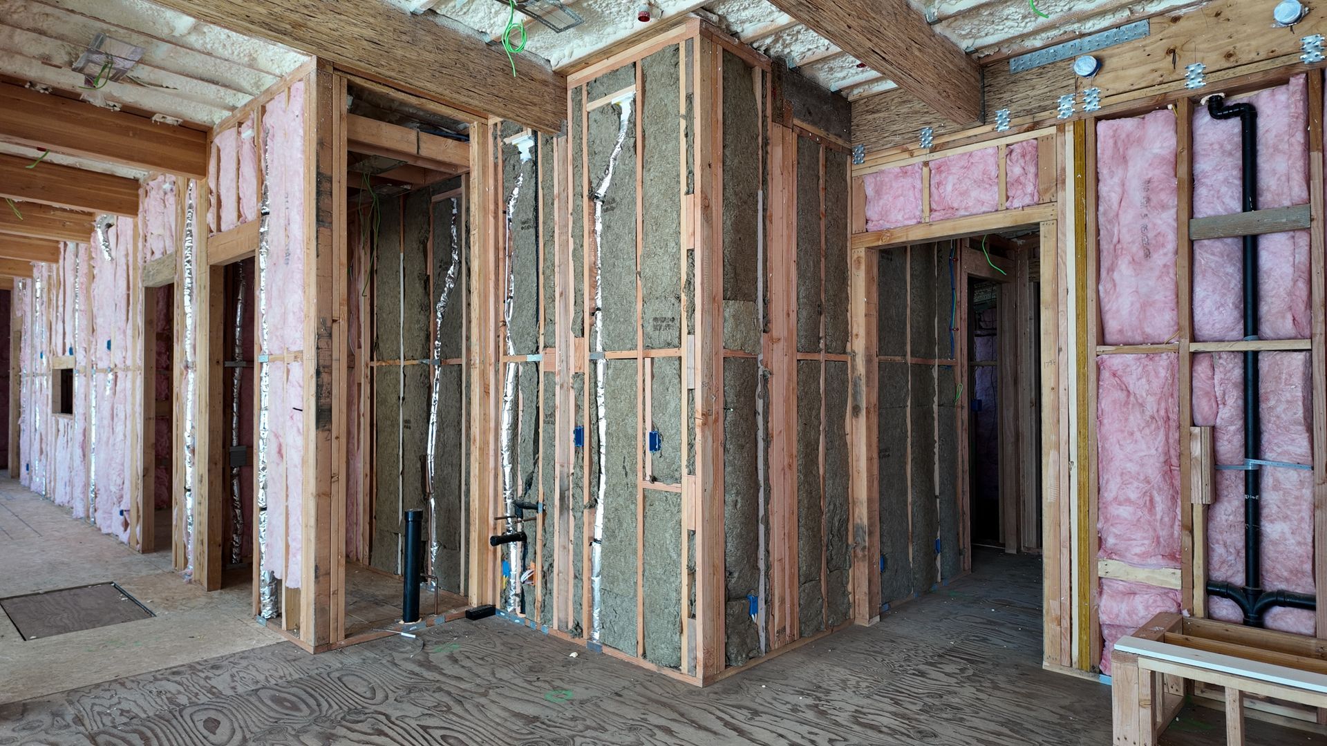 Framed interior of a house under construction, with exposed wood studs and insulation.