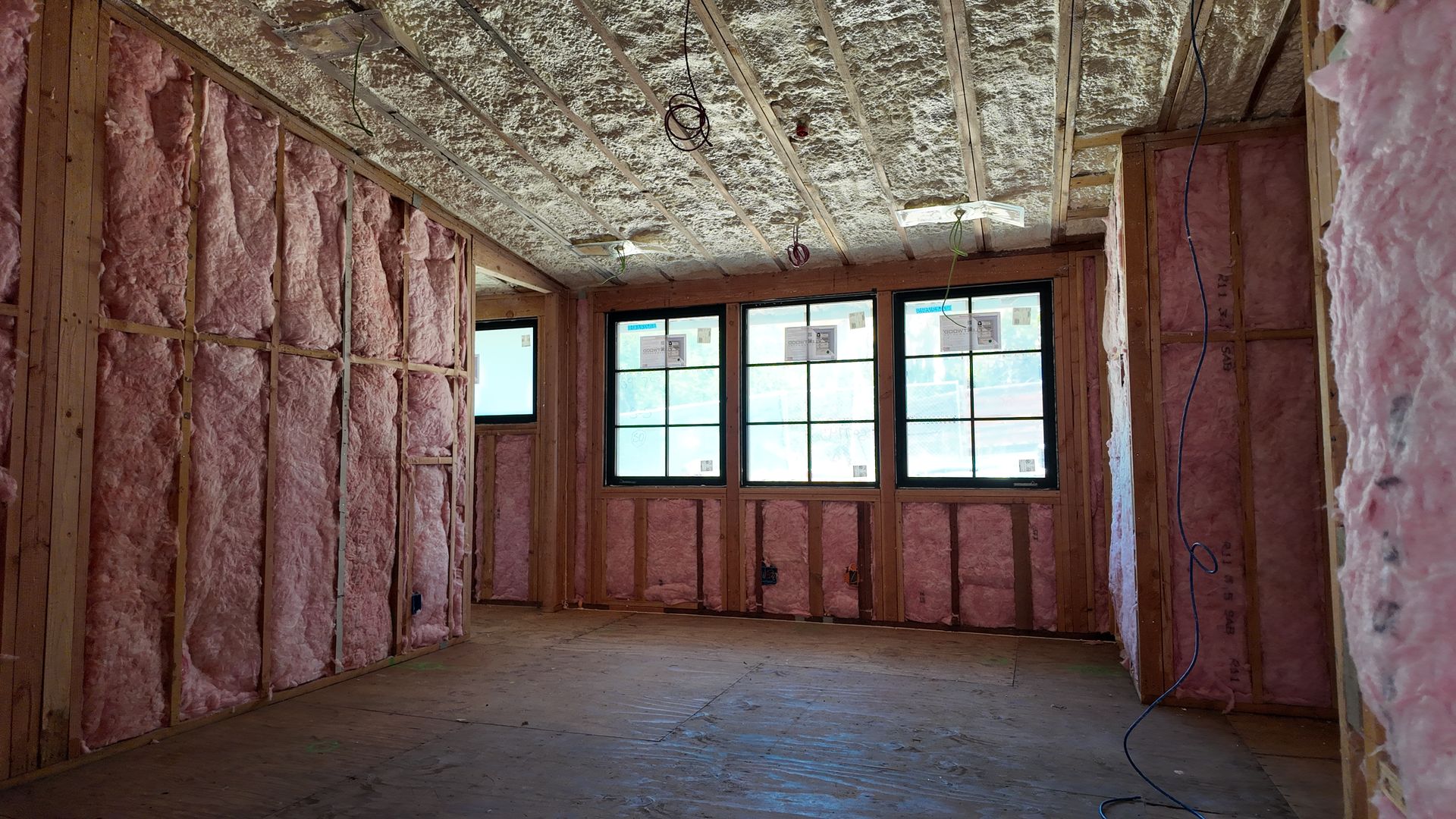 Unfinished room with pink insulation, exposed ceiling, and three windows letting in daylight