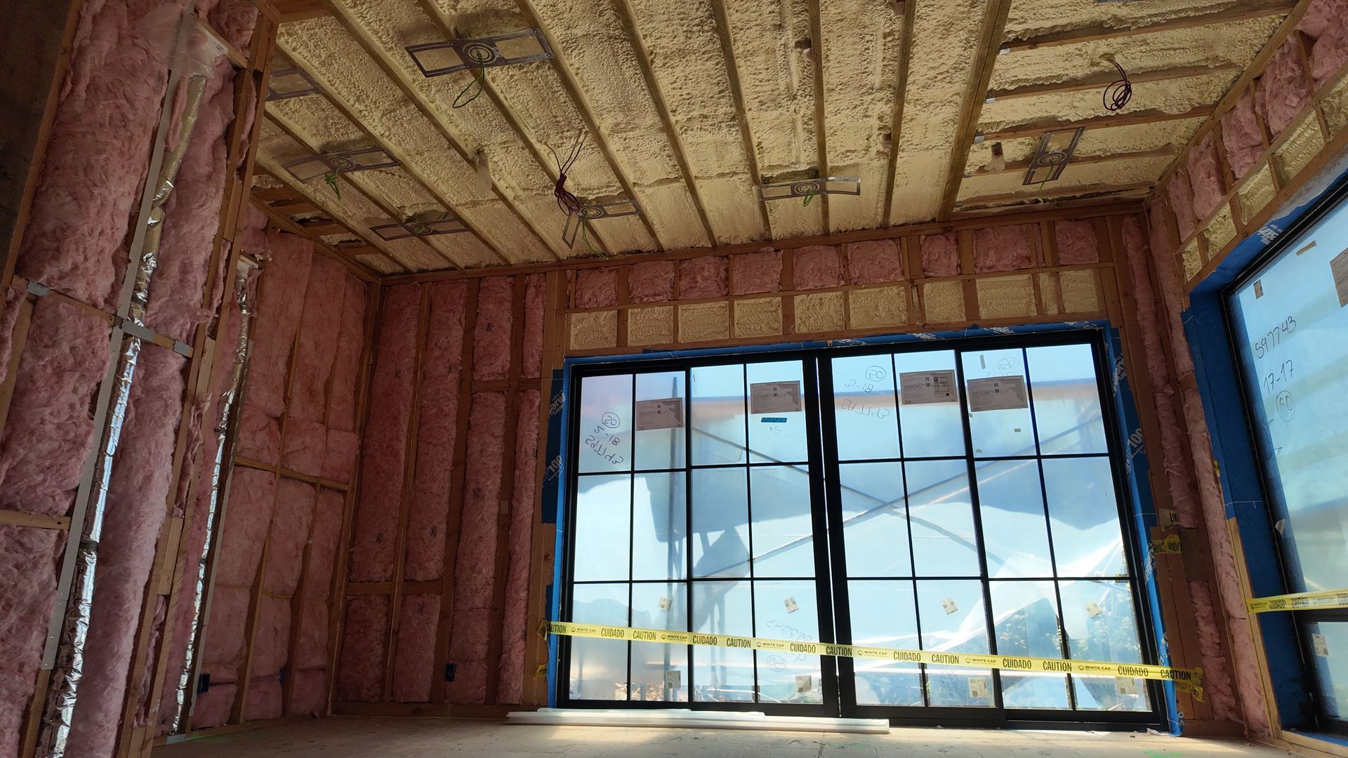 Unfinished room with exposed wood and pink insulation, large window, and bright blue door frame.