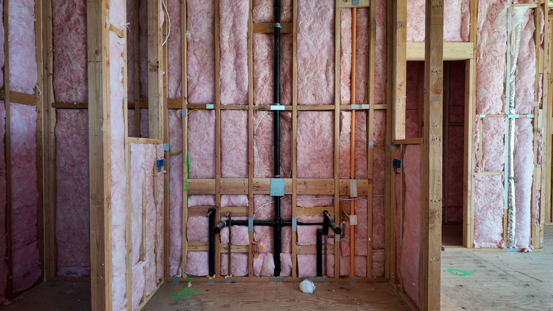 Unfinished room with exposed insulation, wood framing, and plumbing pipes on the wall.