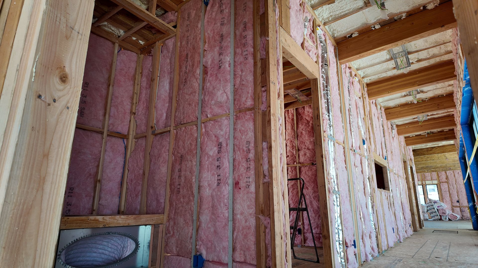 Interior of a house under construction with exposed pink insulation and wooden framing along a hallway