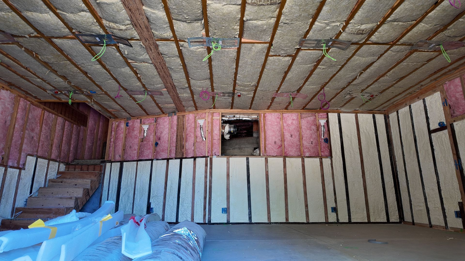 Empty unfinished room with exposed ceiling, pink wall panels, and a staircase on the left.