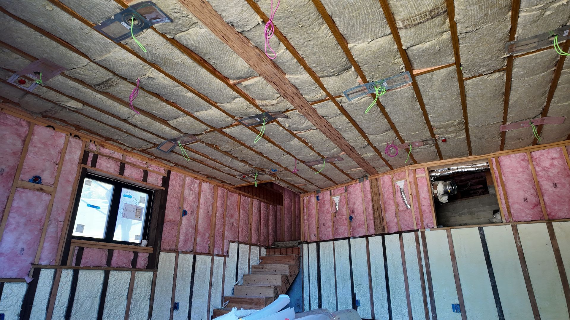 Partially insulated room with exposed framing, pink wall panels, and a window under construction