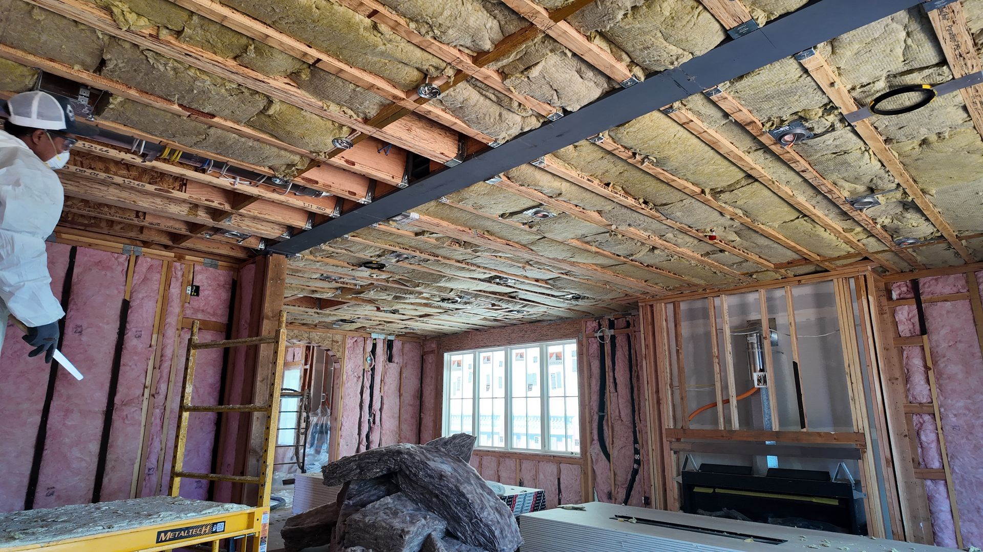 Unfinished room under renovation with exposed insulation, worker on left, and window at the far end