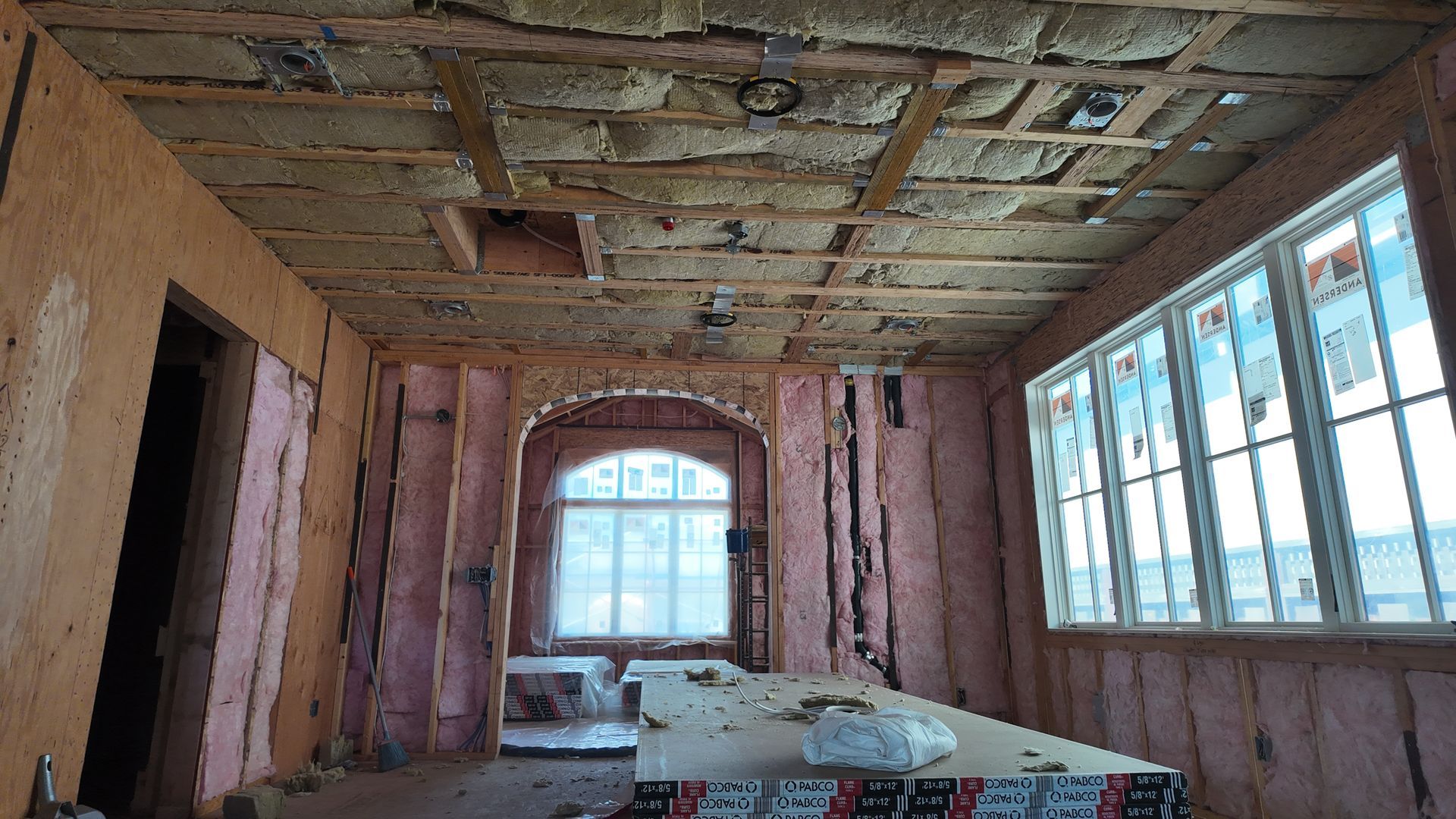 Unfinished room with exposed insulation, large windows, and construction materials on the floor.
