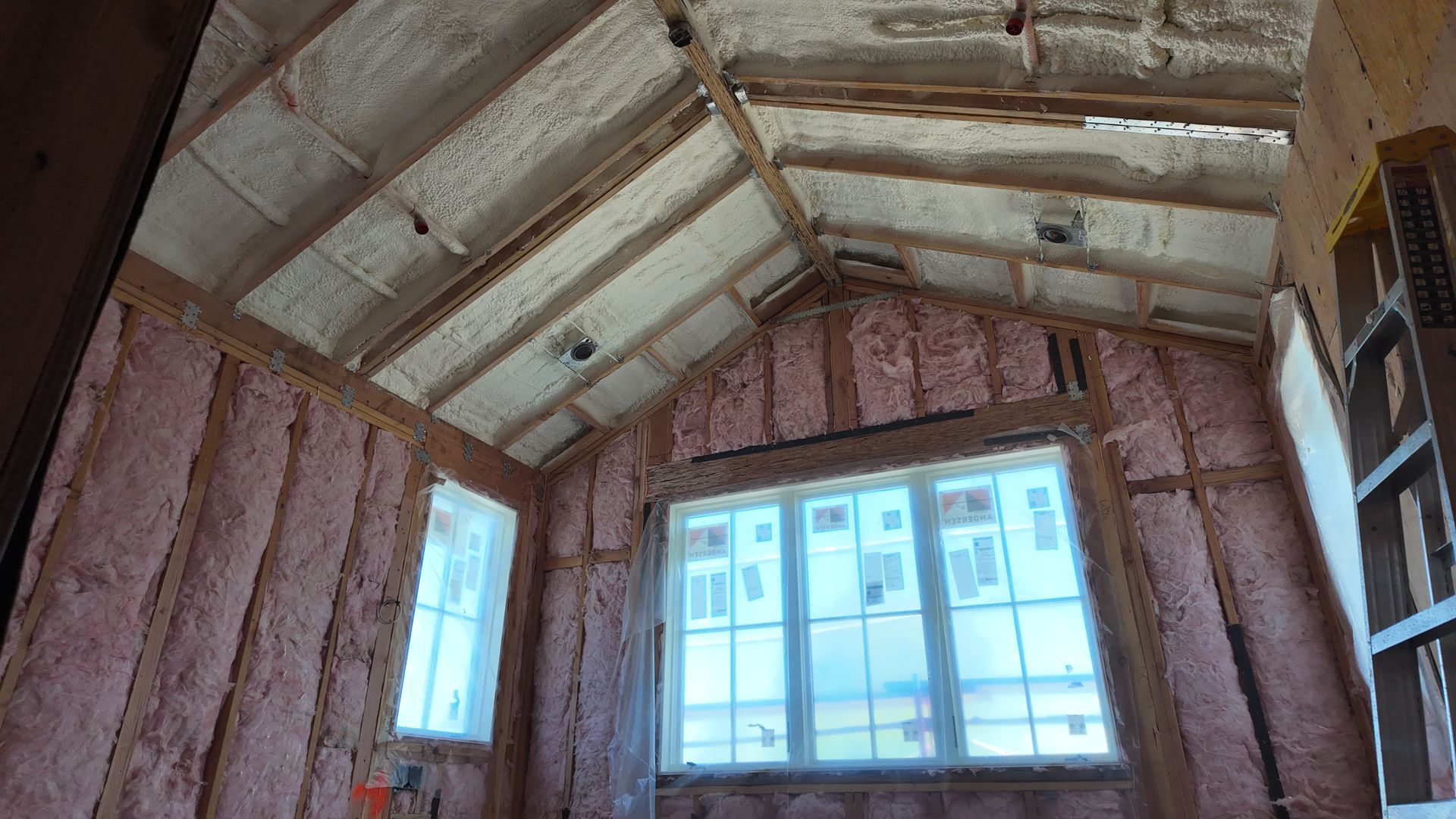 Interior of an unfinished room with pink insulation, exposed beams, and two windows.