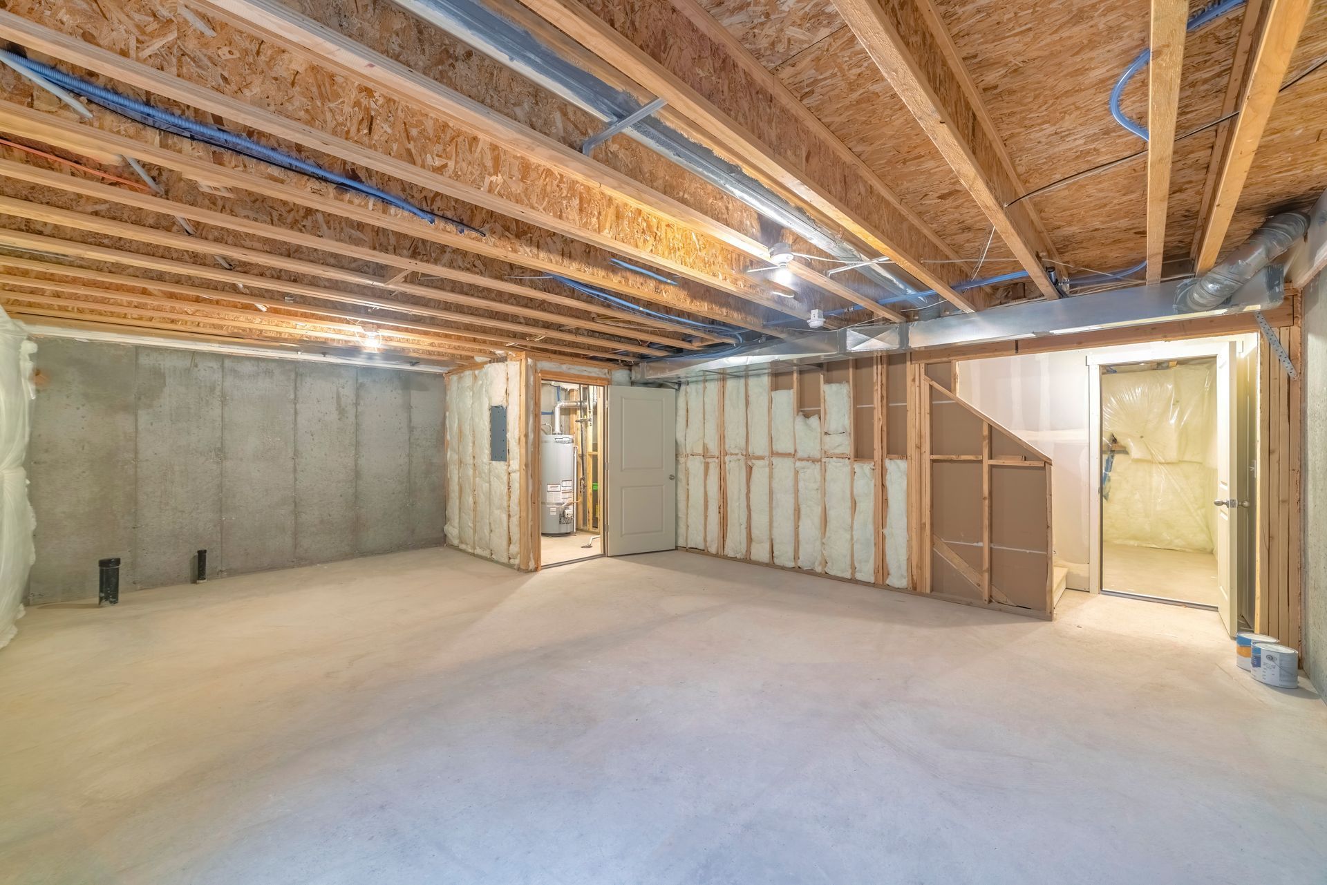 Unfinished basement with exposed wooden joists, concrete walls, and drywall in progress