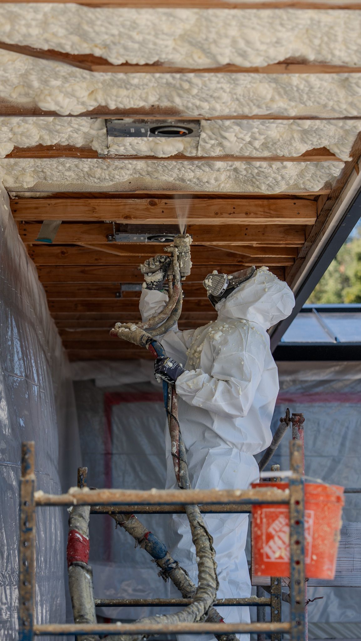 Worker installing insulation in an attic with exposed wooden beams and HVAC ductwork.