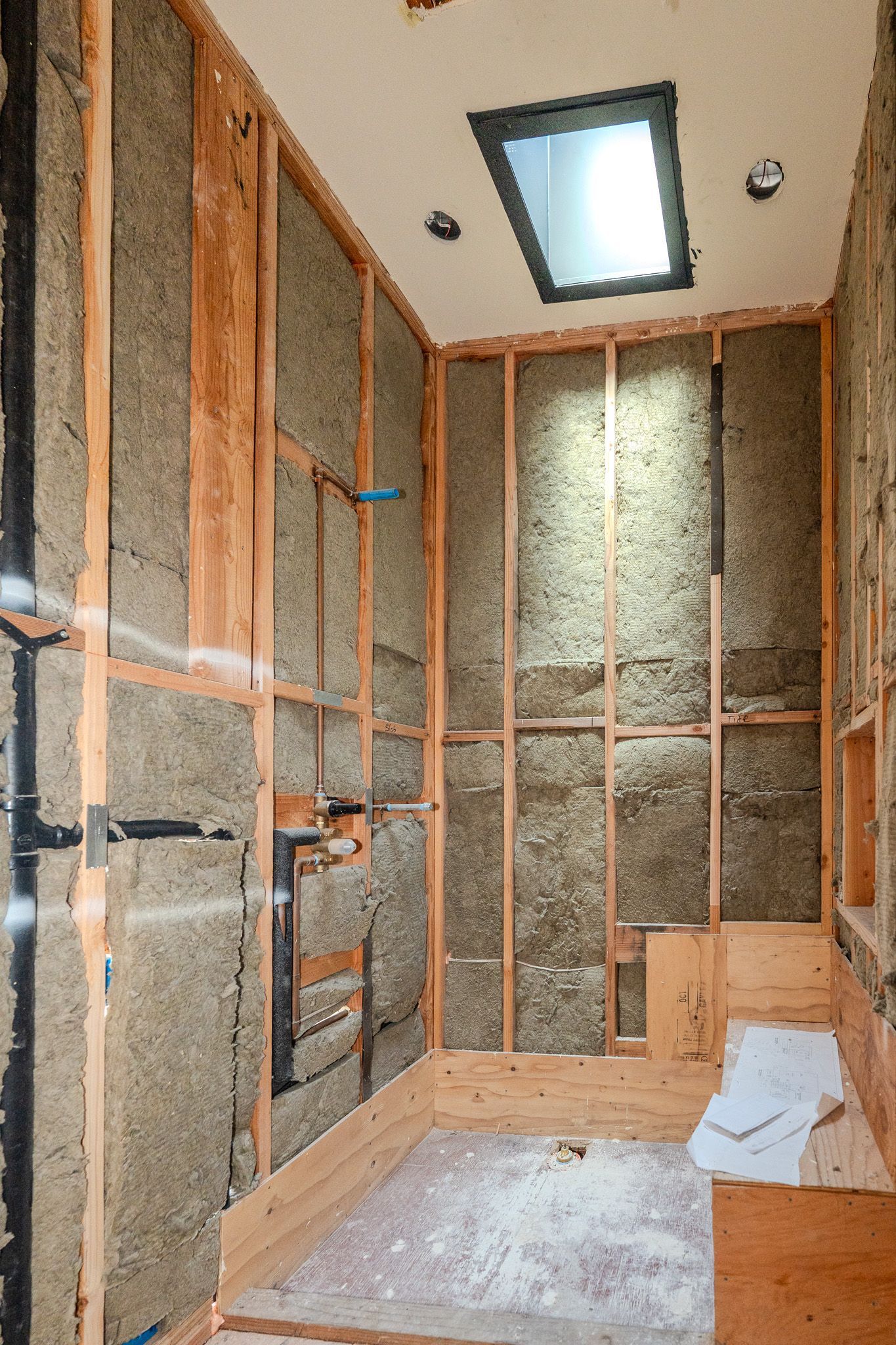 Insulated ceiling with white spray foam, exposed wooden beams, and brick wall corner under construction