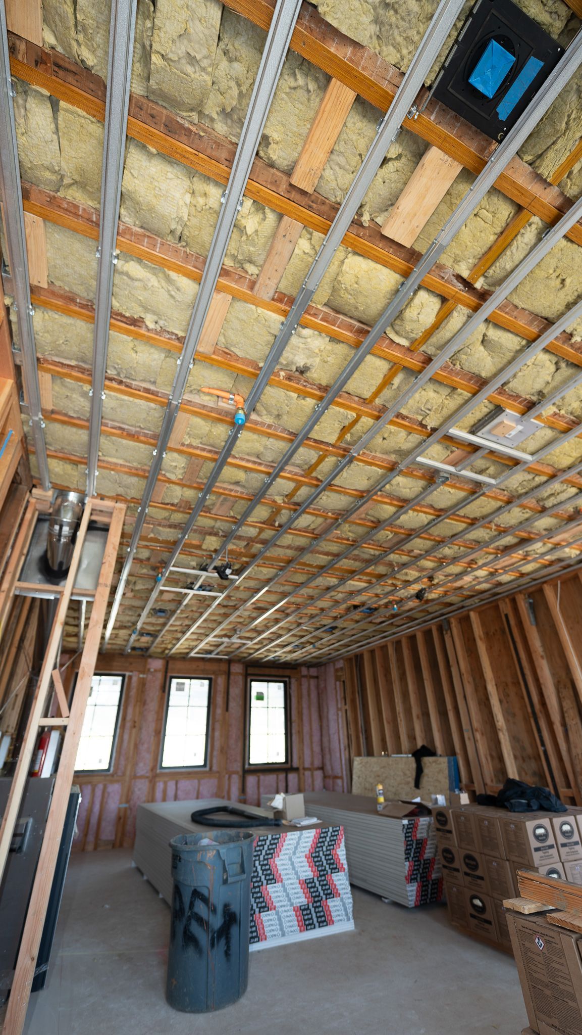Unfinished room with exposed ceiling insulation, framed walls, windows, and stacked construction materials.