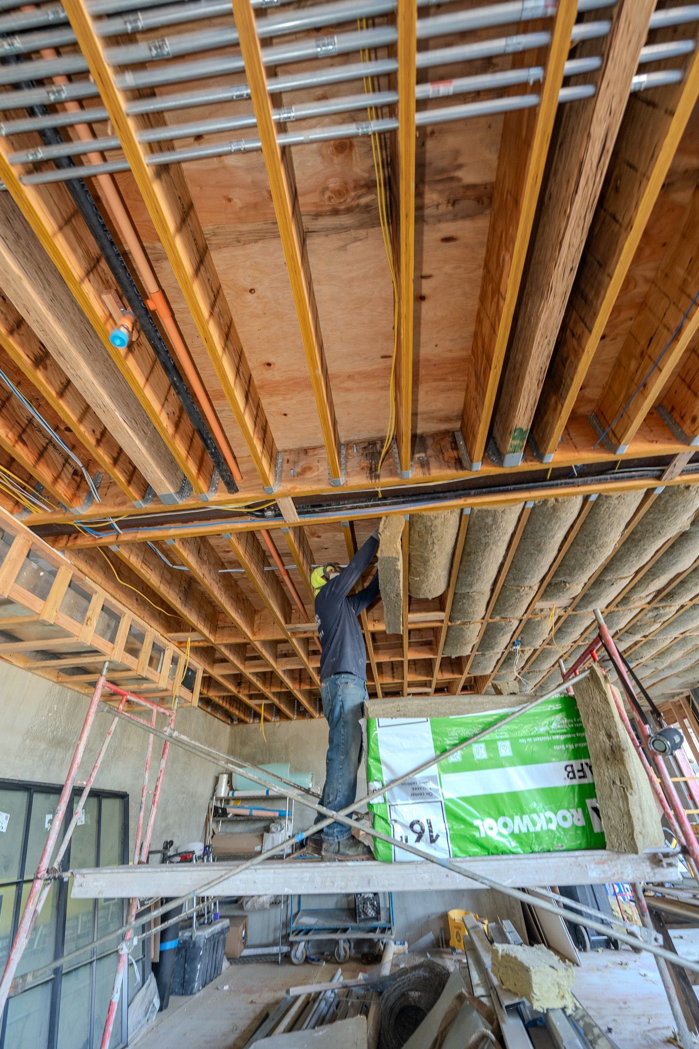Worker in white protective suit installing yellow insulation inside a framed wall