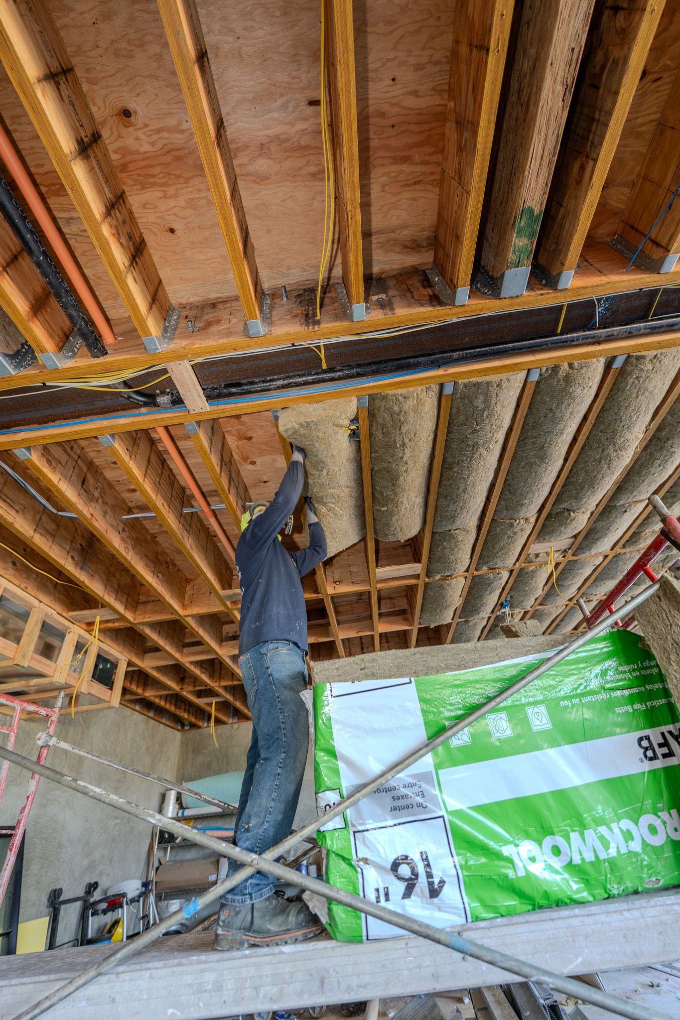 Worker spray-foaming insulation on a ceiling inside a house under construction.