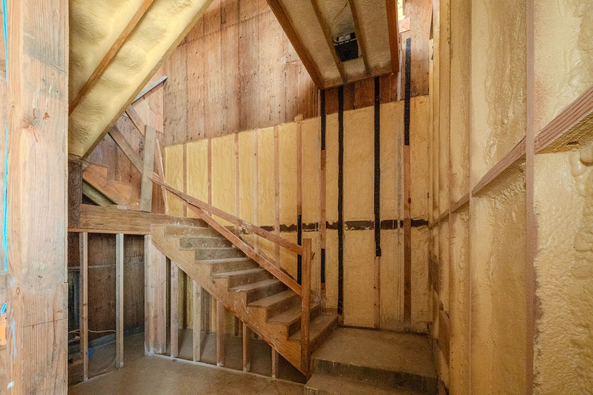 Wooden staircase in an unfinished attic with exposed beams and walls