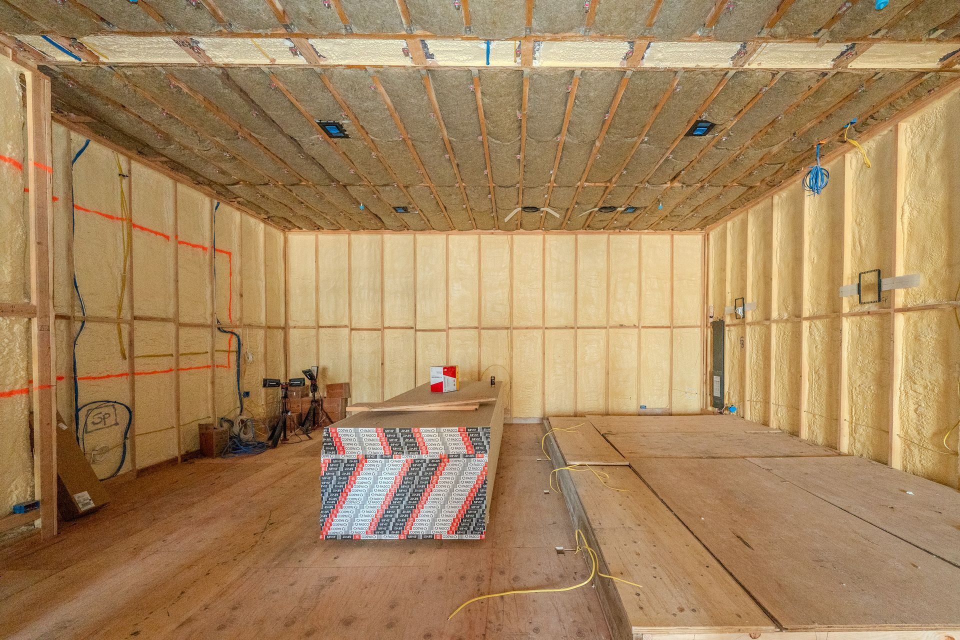 Worker in protective suit applying material to a floor in an unfinished room, with a yellow bag nearby