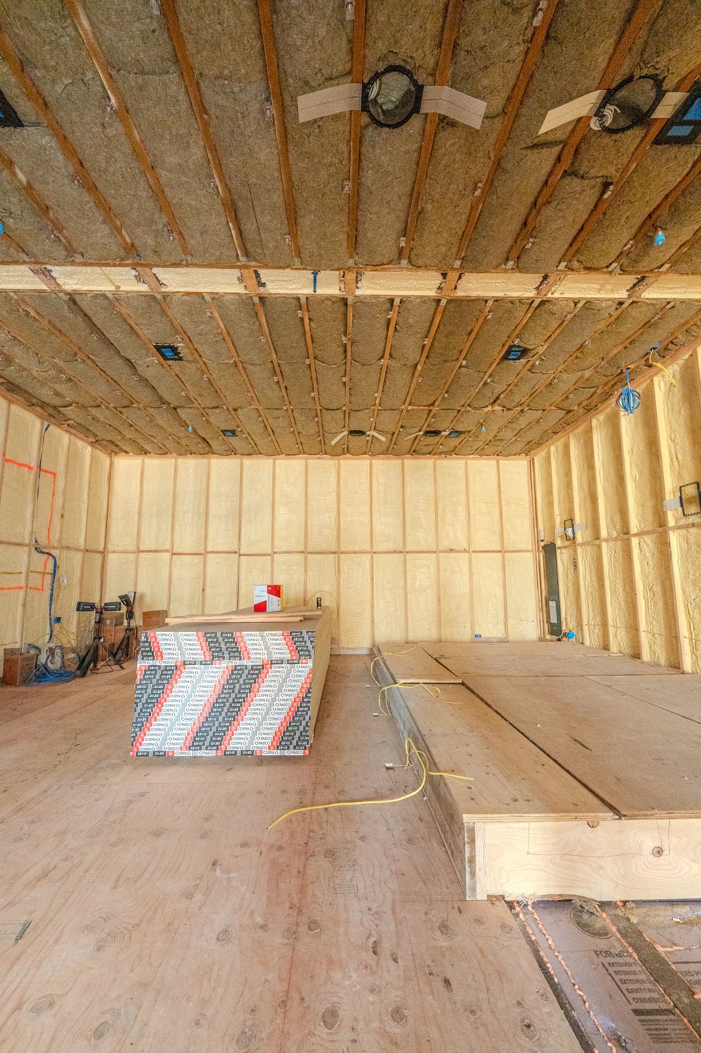 Unfinished attic roof framing with exposed wooden trusses and insulation around a small window.