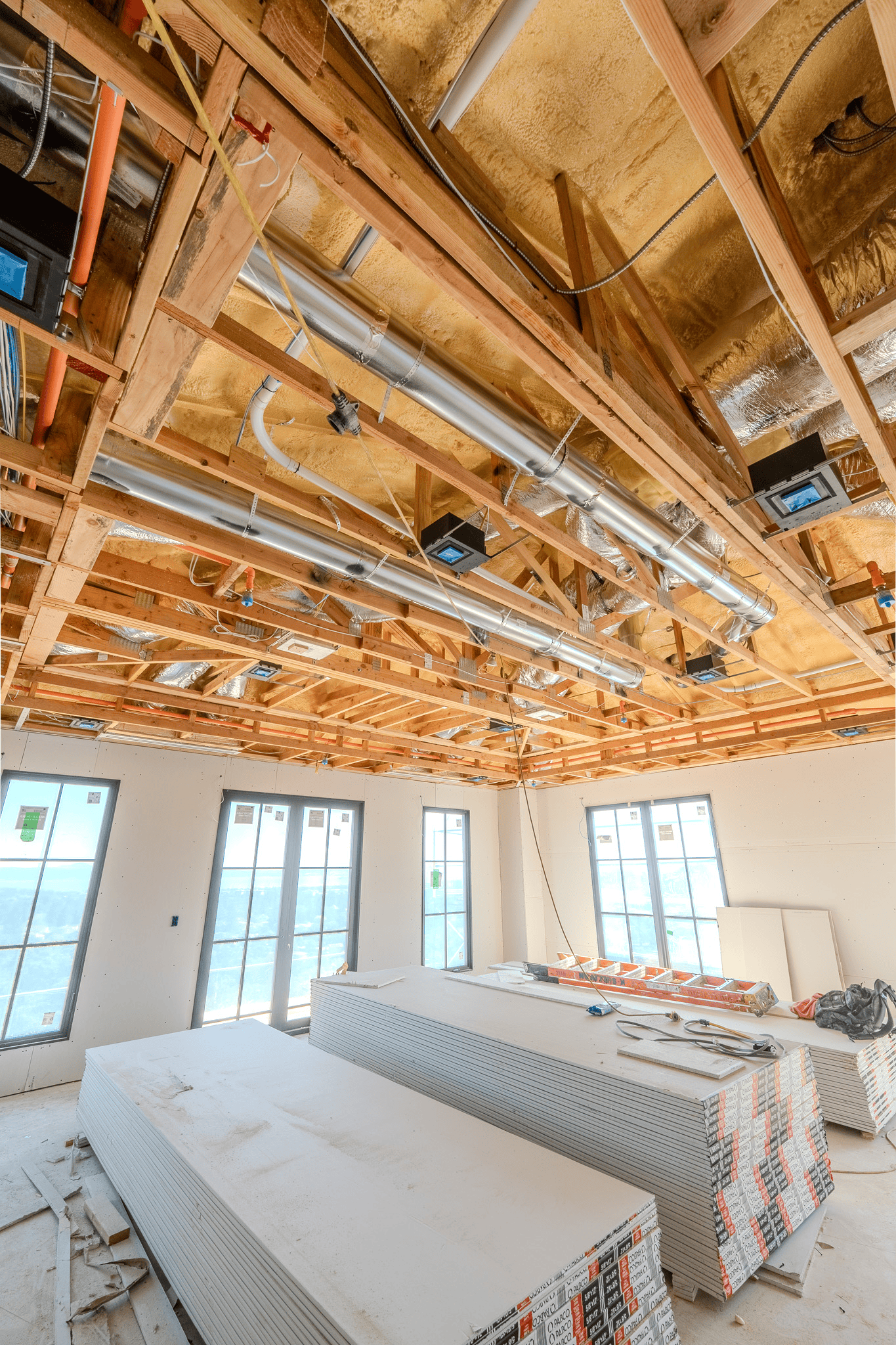 Worker spray-insulating a wooden wall frame inside a house under construction