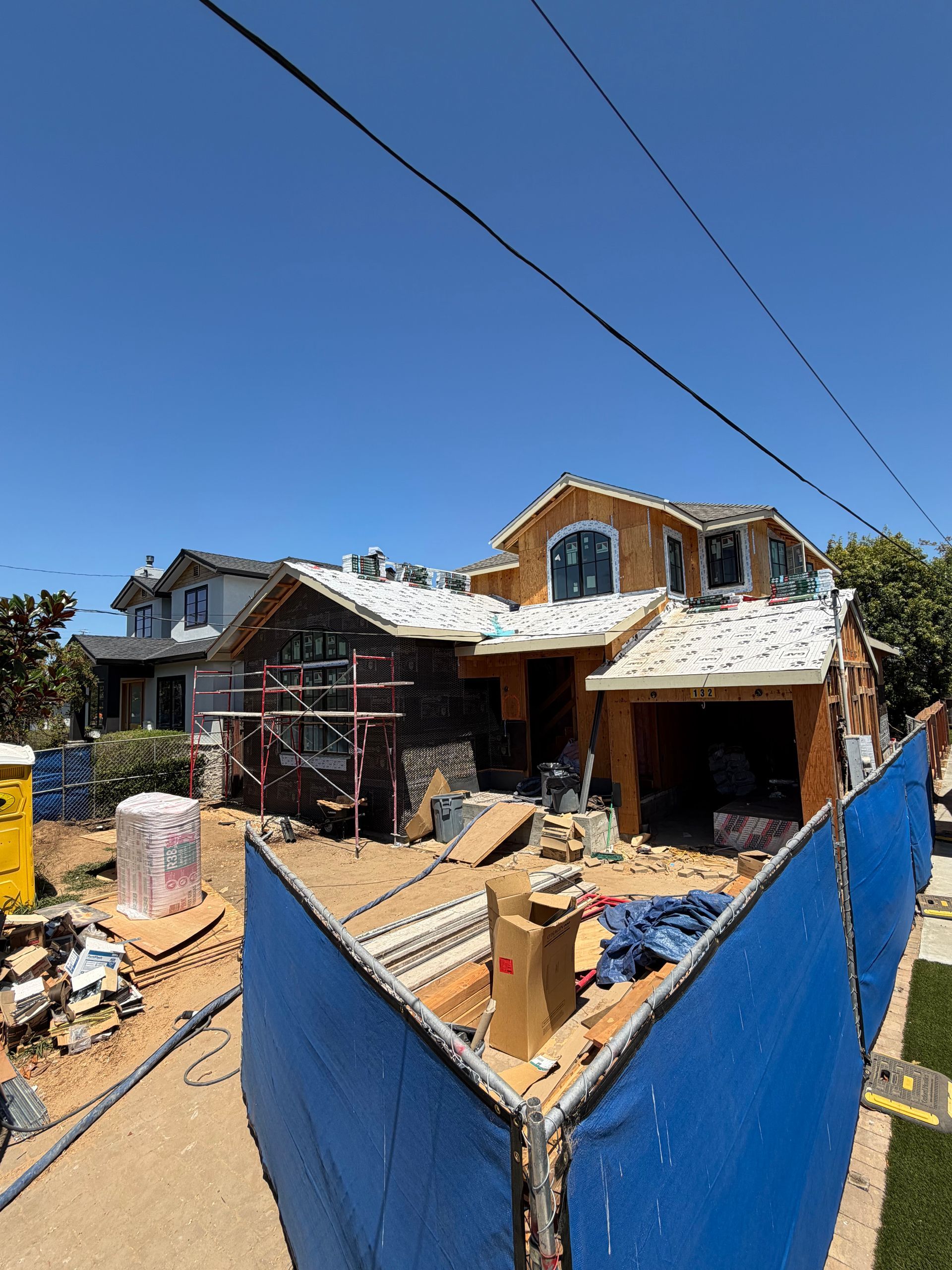 Damaged house under construction with blue temporary fence and debris in front