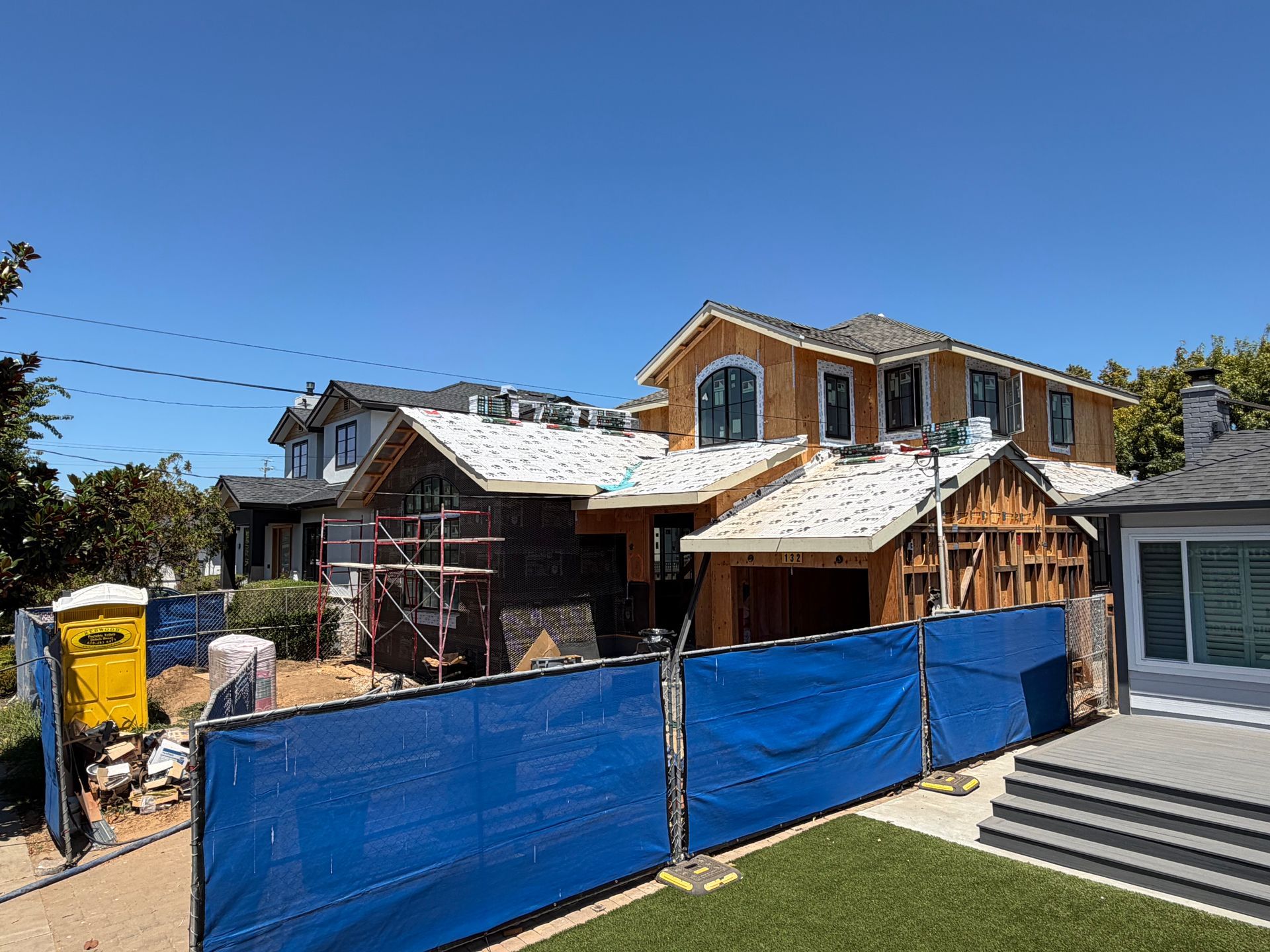 House under construction with blue tarp fence and workers’ debris under a clear blue sky
