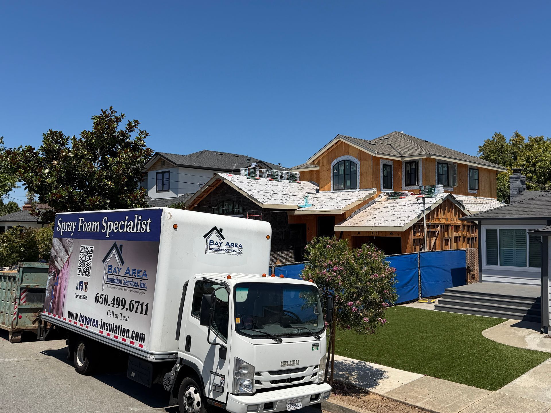 Moving truck parked outside a house under construction with blue tarp and exposed framing
