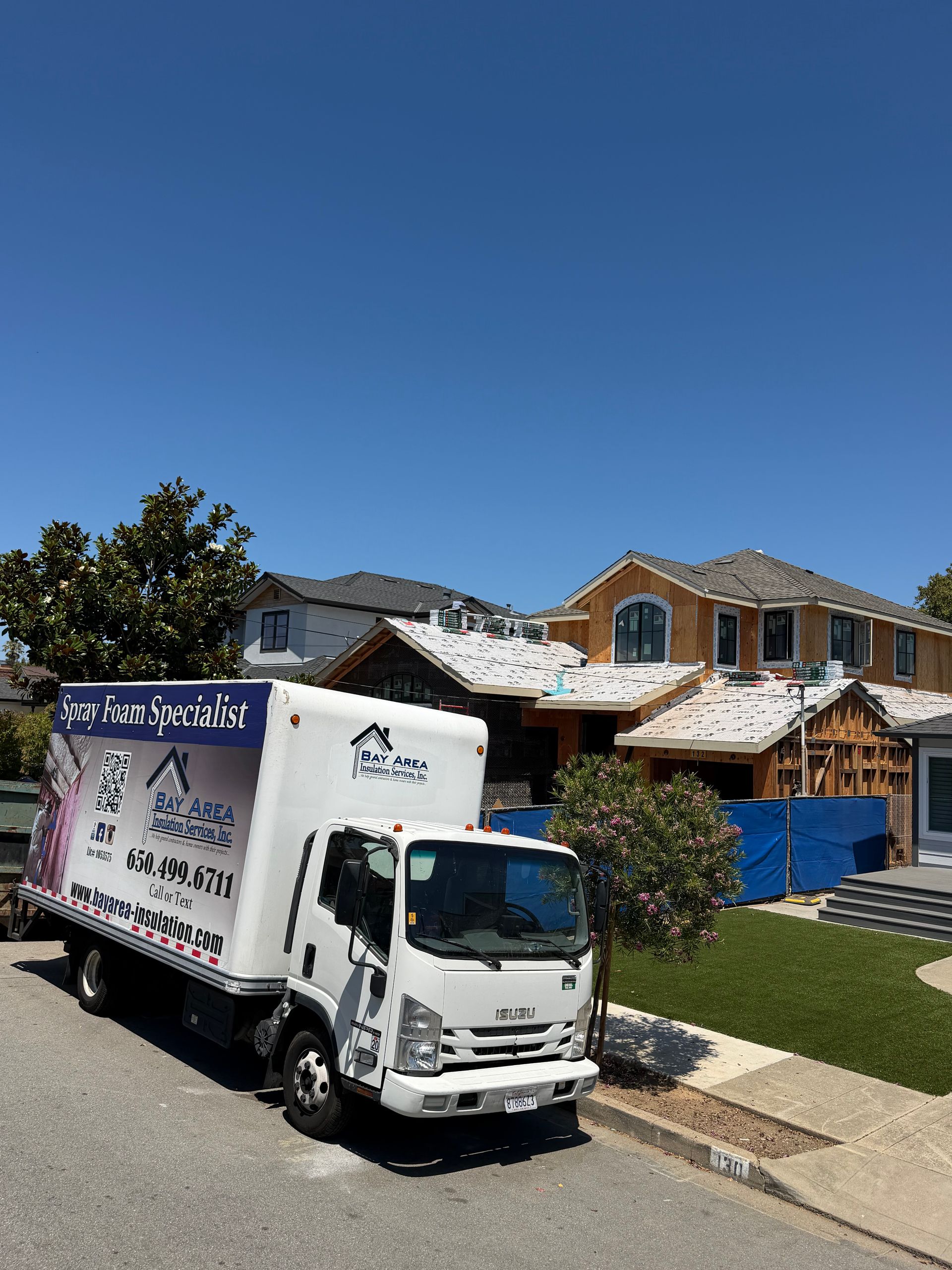 White delivery truck parked on a suburban street in front of new houses under a clear blue sky