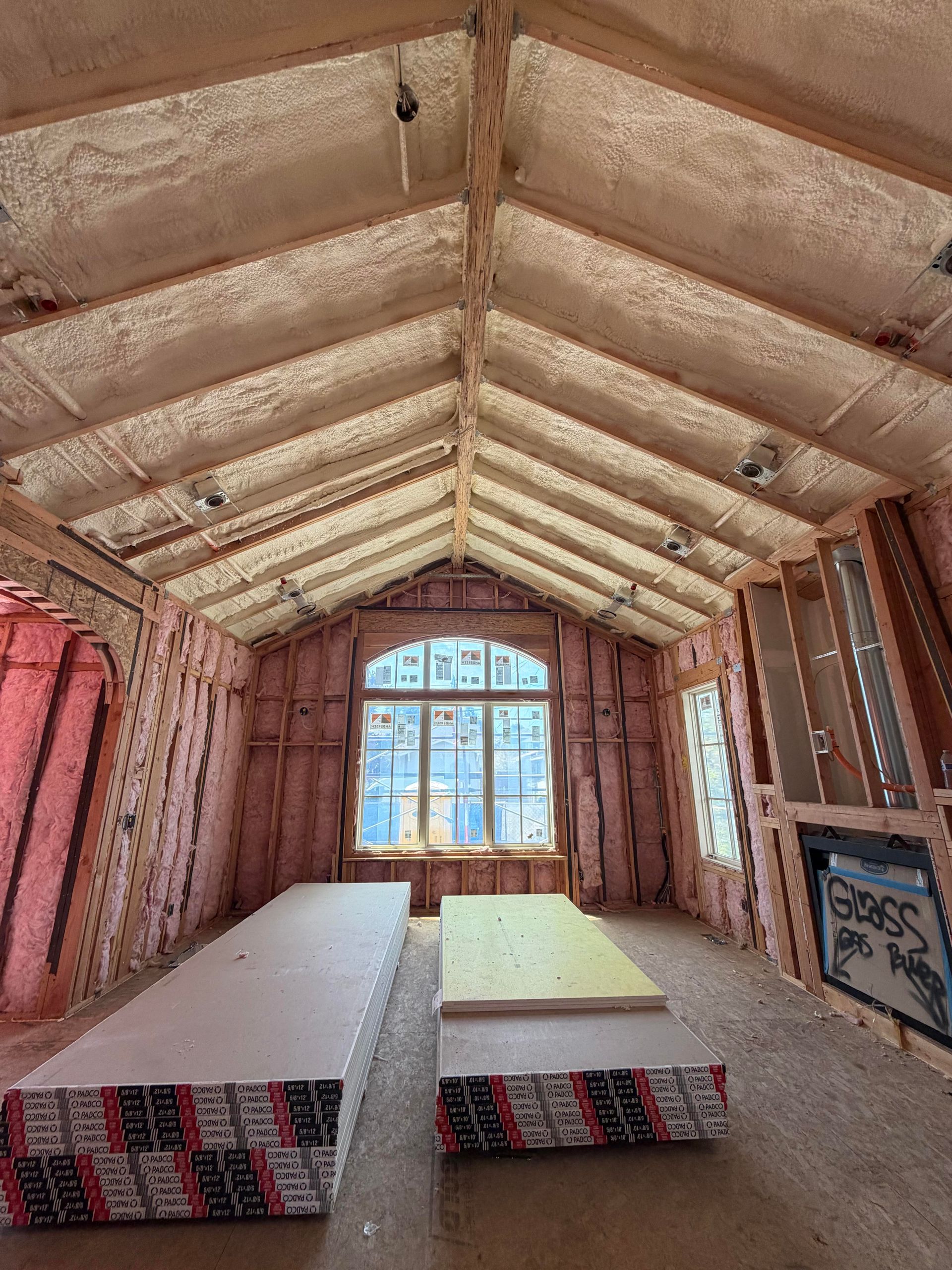 Unfinished insulated room with vaulted ceiling, two mattresses on the floor, and a window at the far end.