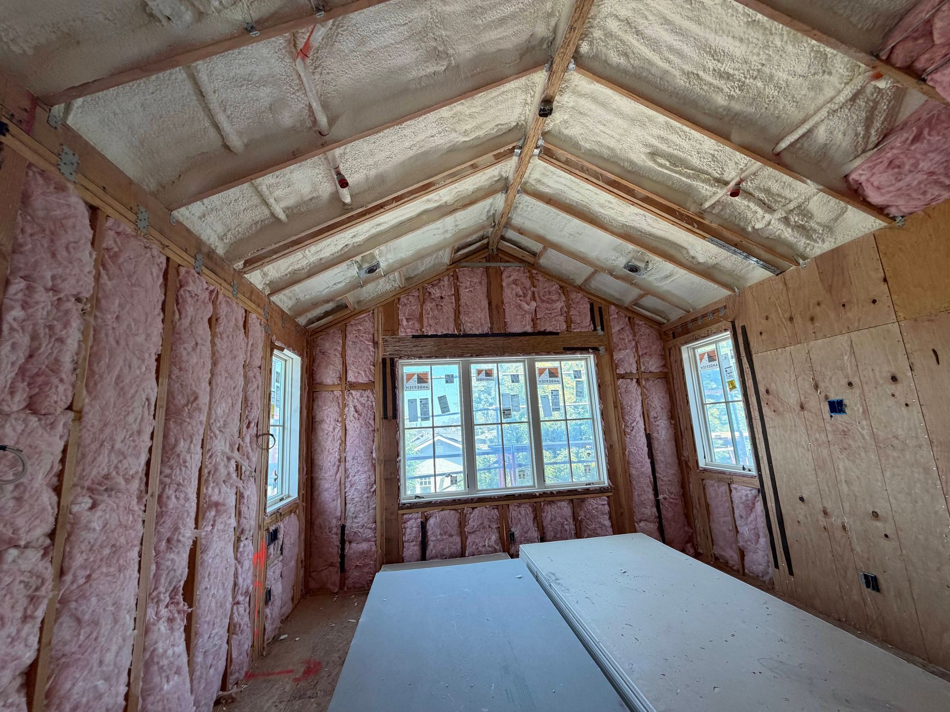 Unfinished room with pink insulation, exposed rafters, and windows at the far end