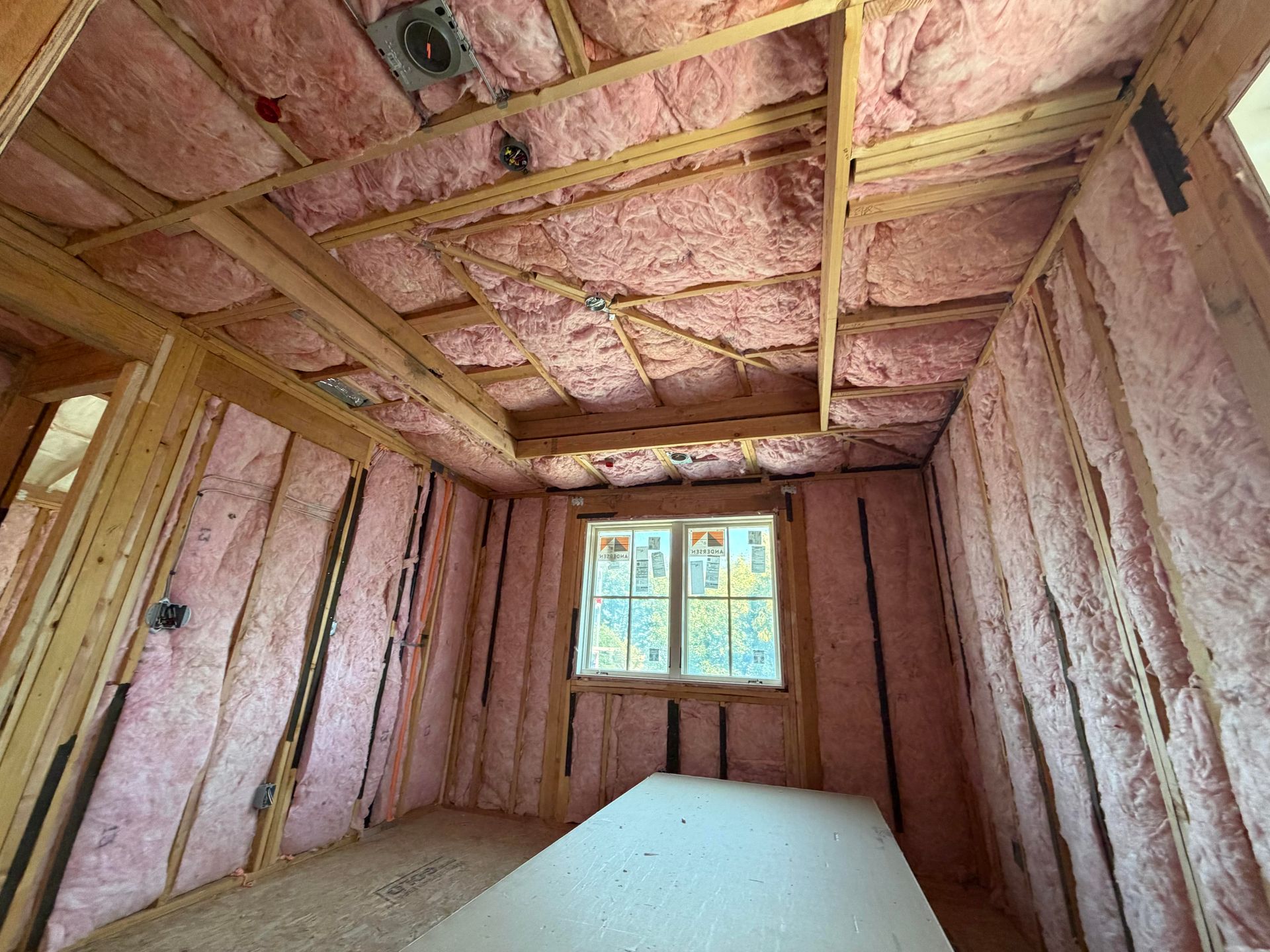 Insulated unfinished room with exposed wooden framing and a window at the far end