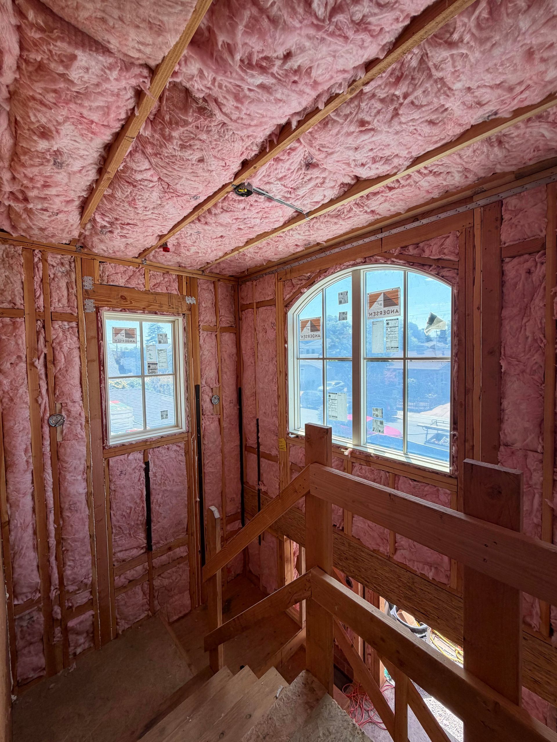 Unfinished room with pink insulation, wooden framing, and windows overlooking a snowy outdoor scene