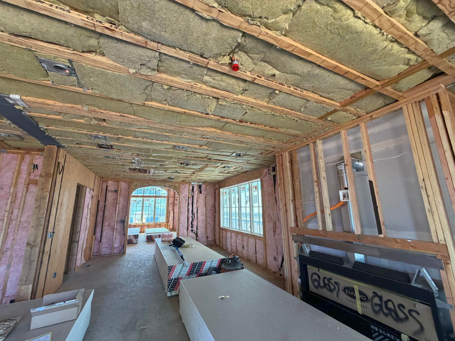 Unfinished room under construction with exposed insulation, wood framing, and windows at both ends.