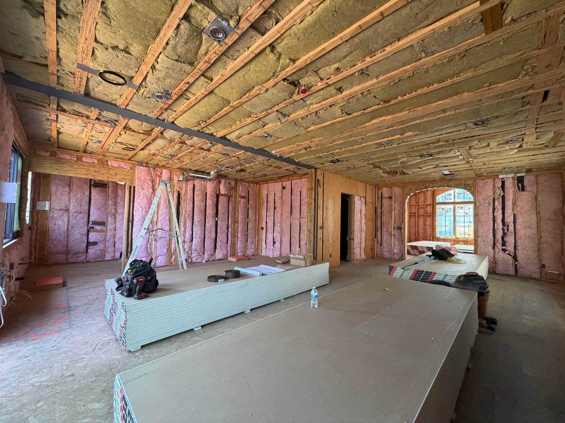Unfinished room with exposed insulation, pink wall framing, and scattered construction materials.