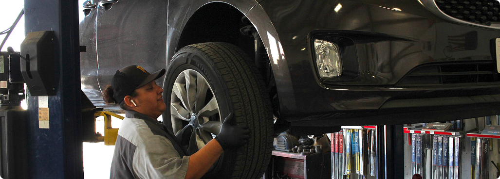 Car repair shop interior with a vehicle lifted on a hydraulic lift. A second vehicle and various tools are visible.