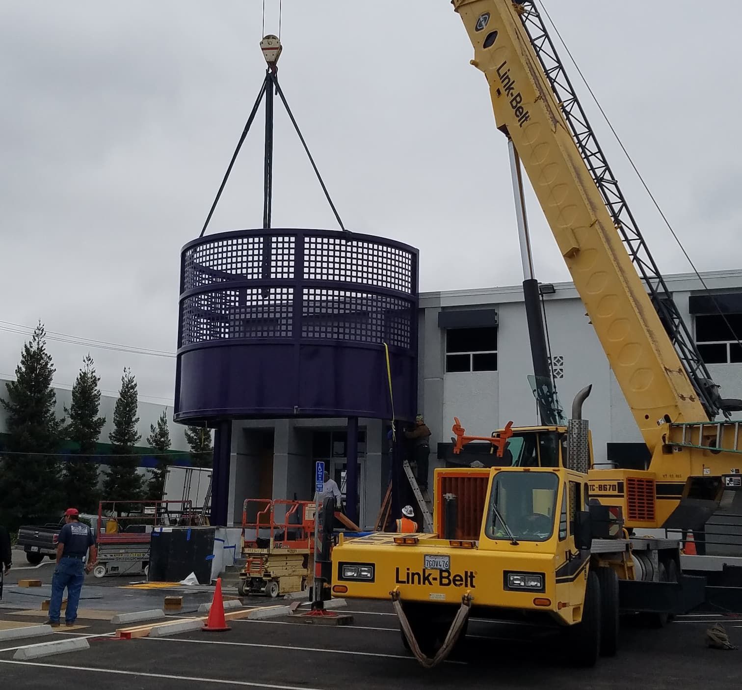 A powder-coated architectural fixture being lifted into place by a crane for a commercial building