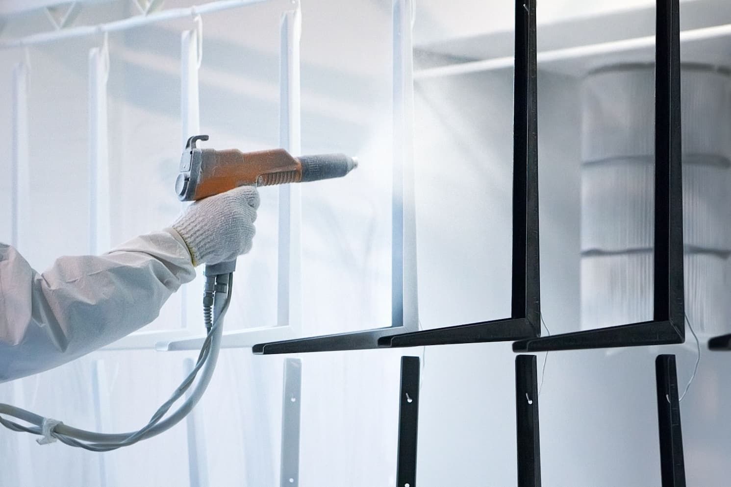 A technician using an electrostatic spray gun to apply powder coating on a metal part